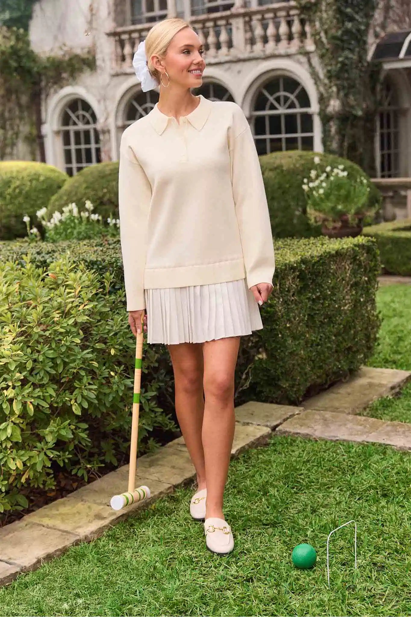 Woman playing croquet in a formal setting with a mansion in the background