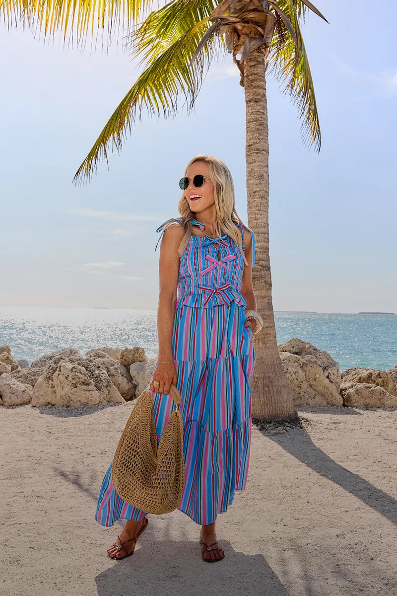 Woman in a colorful striped dress standing on a beach with palm trees and ocean in the background. mobile