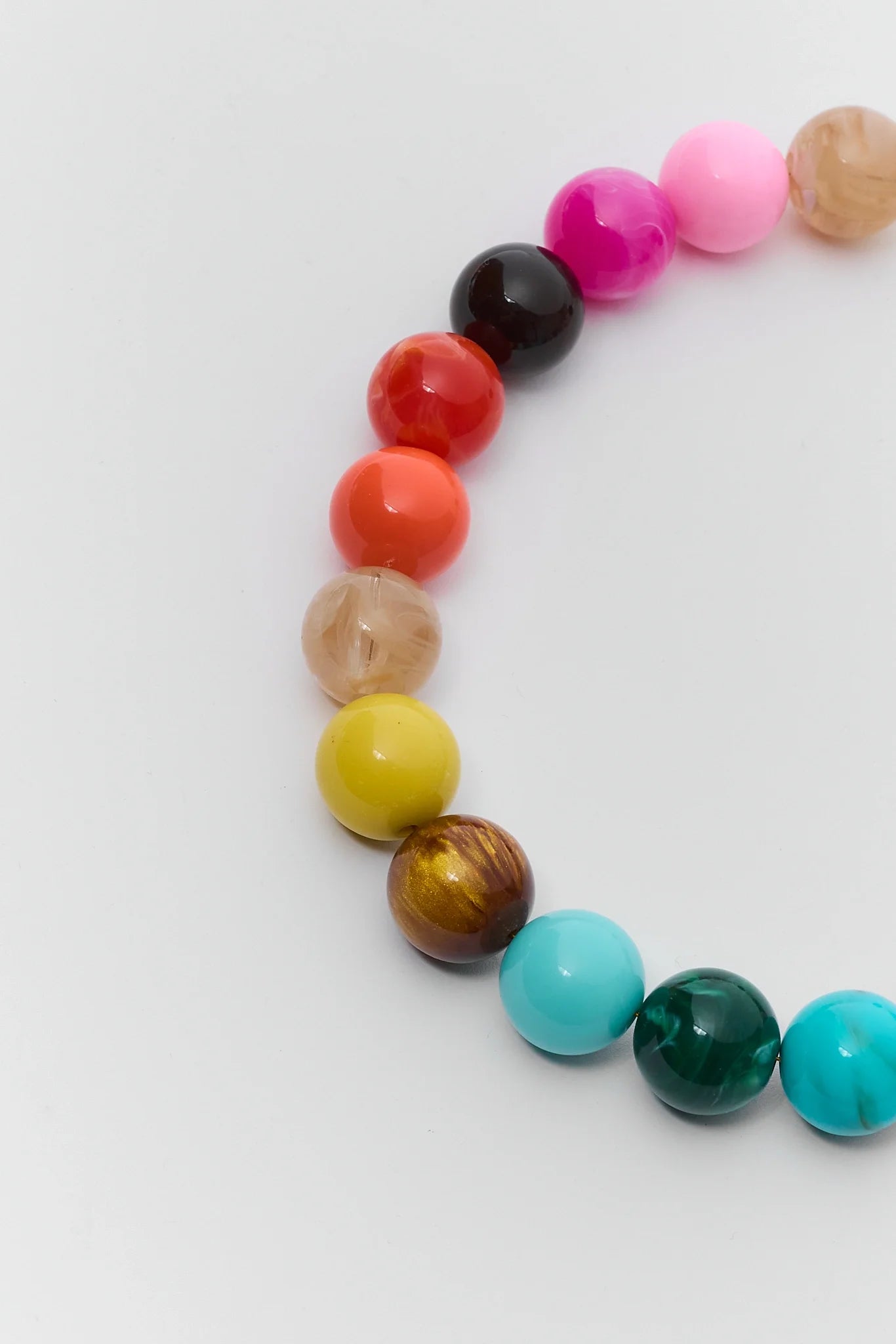 A strand of colorful round beads arranged in a curve on a plain light background. The beads include pink, black, red, orange, beige, yellow, brown, turquoise, and dark green.