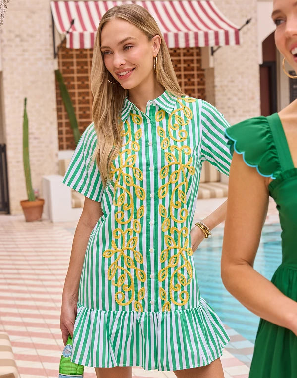 Woman wearing a green and white striped dress with yellow chain pattern by a poolside. navigation
