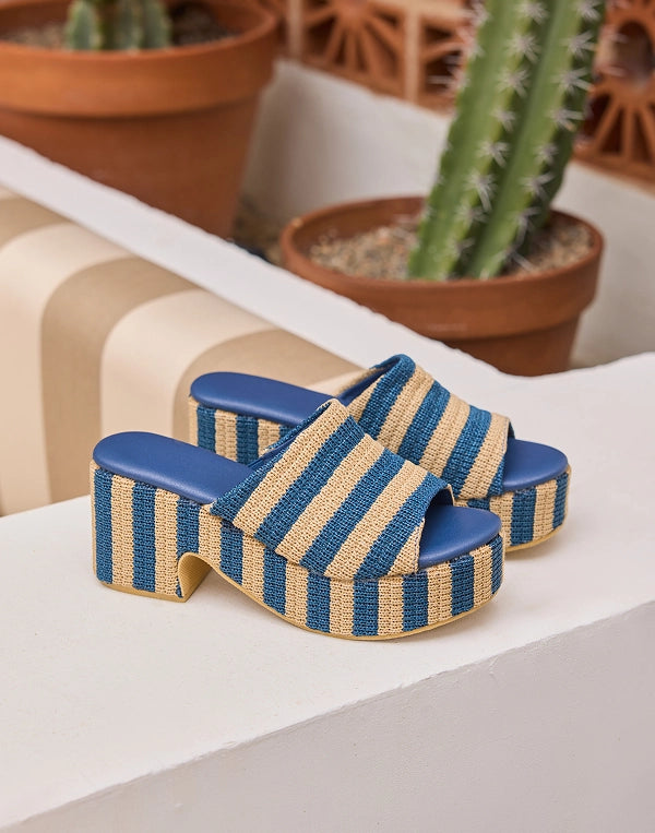 Blue and beige striped platform sandals on a white surface with cacti in the background NAVIGATION