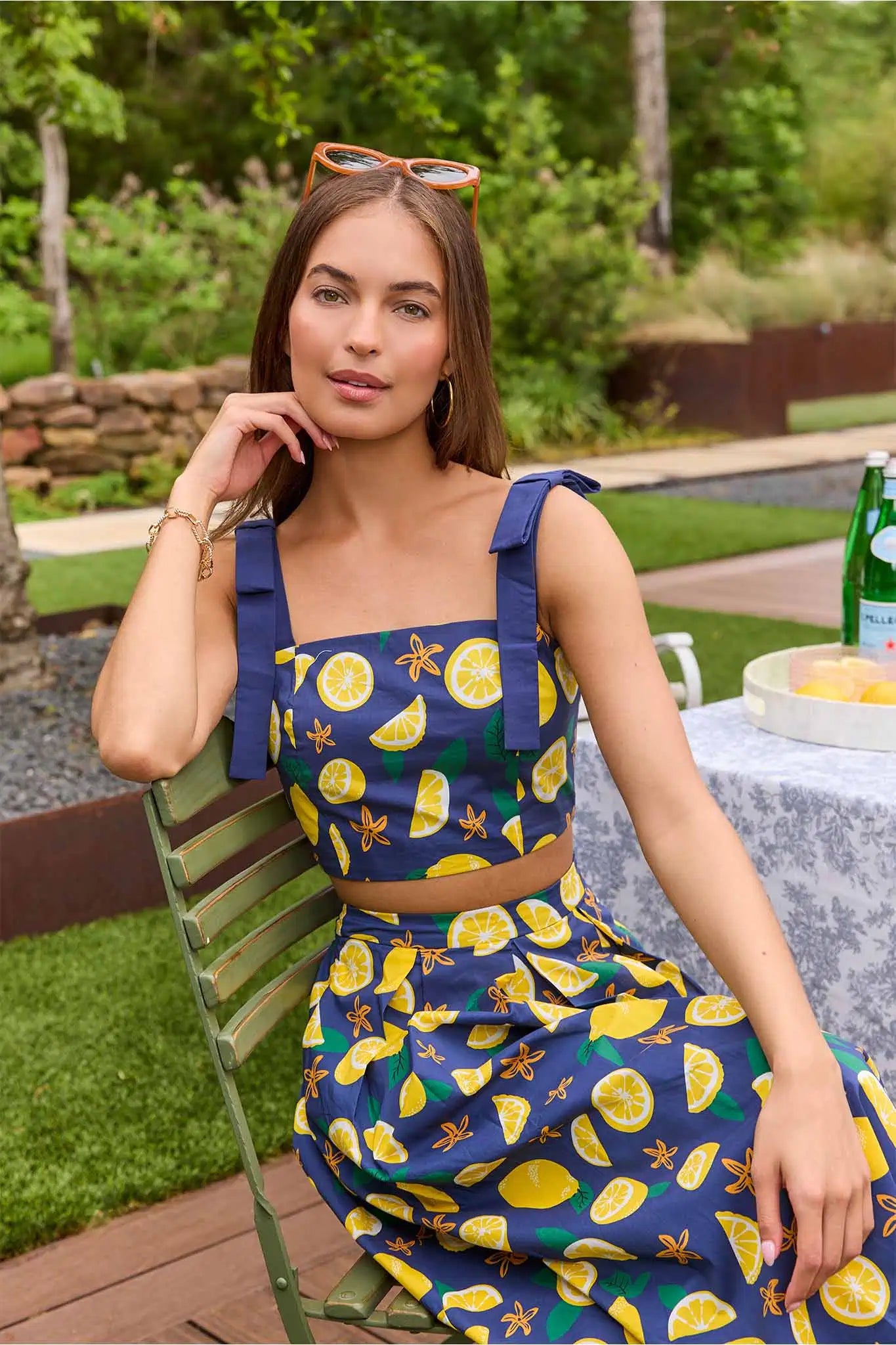 Woman wearing a blue dress with lemon pattern sitting outdoors.