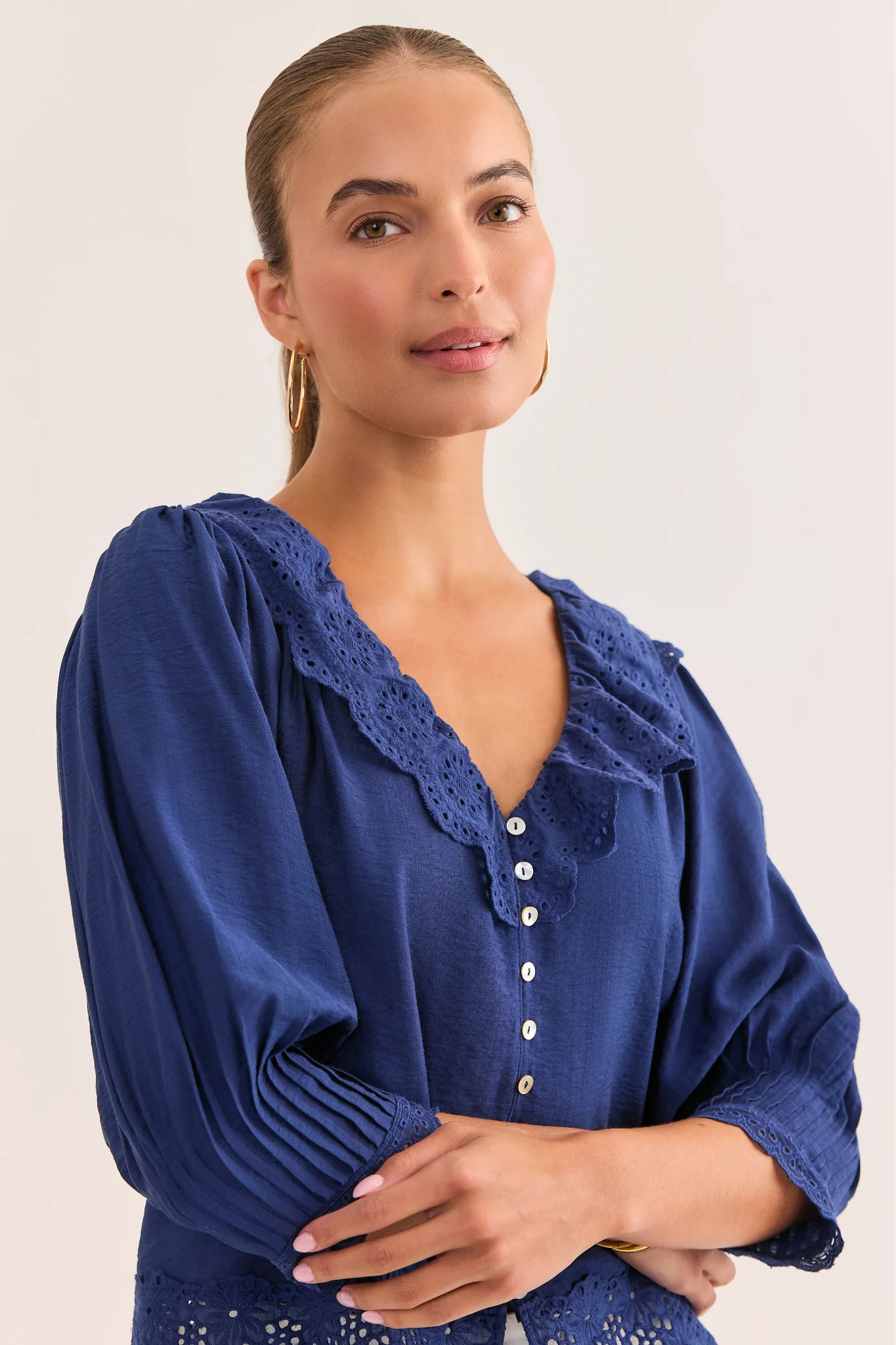 Woman wearing a blue blouse with lace details on a plain background close up