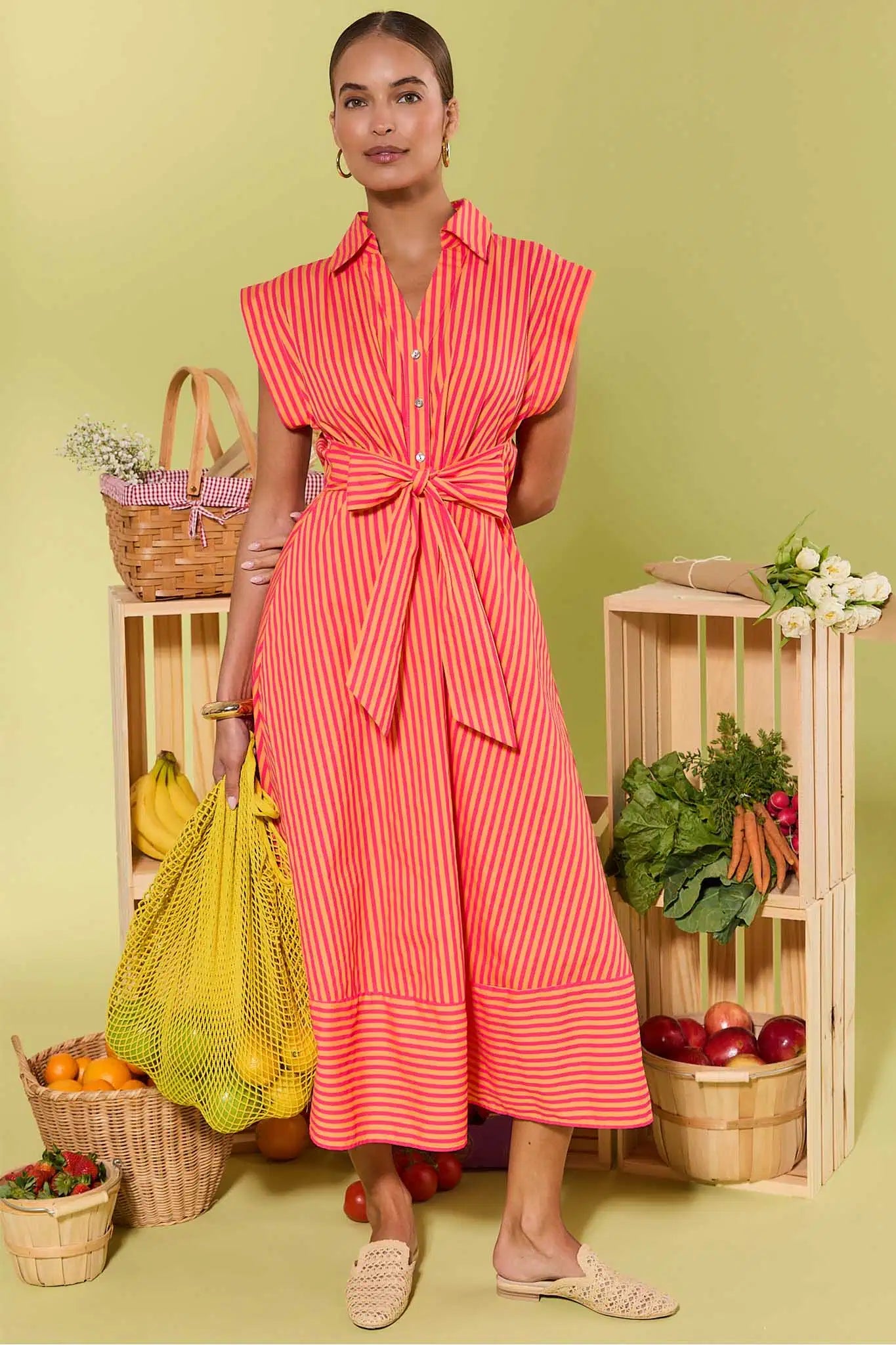 Woman in a red and white striped dress standing in front of wooden crates with groceries on a green background