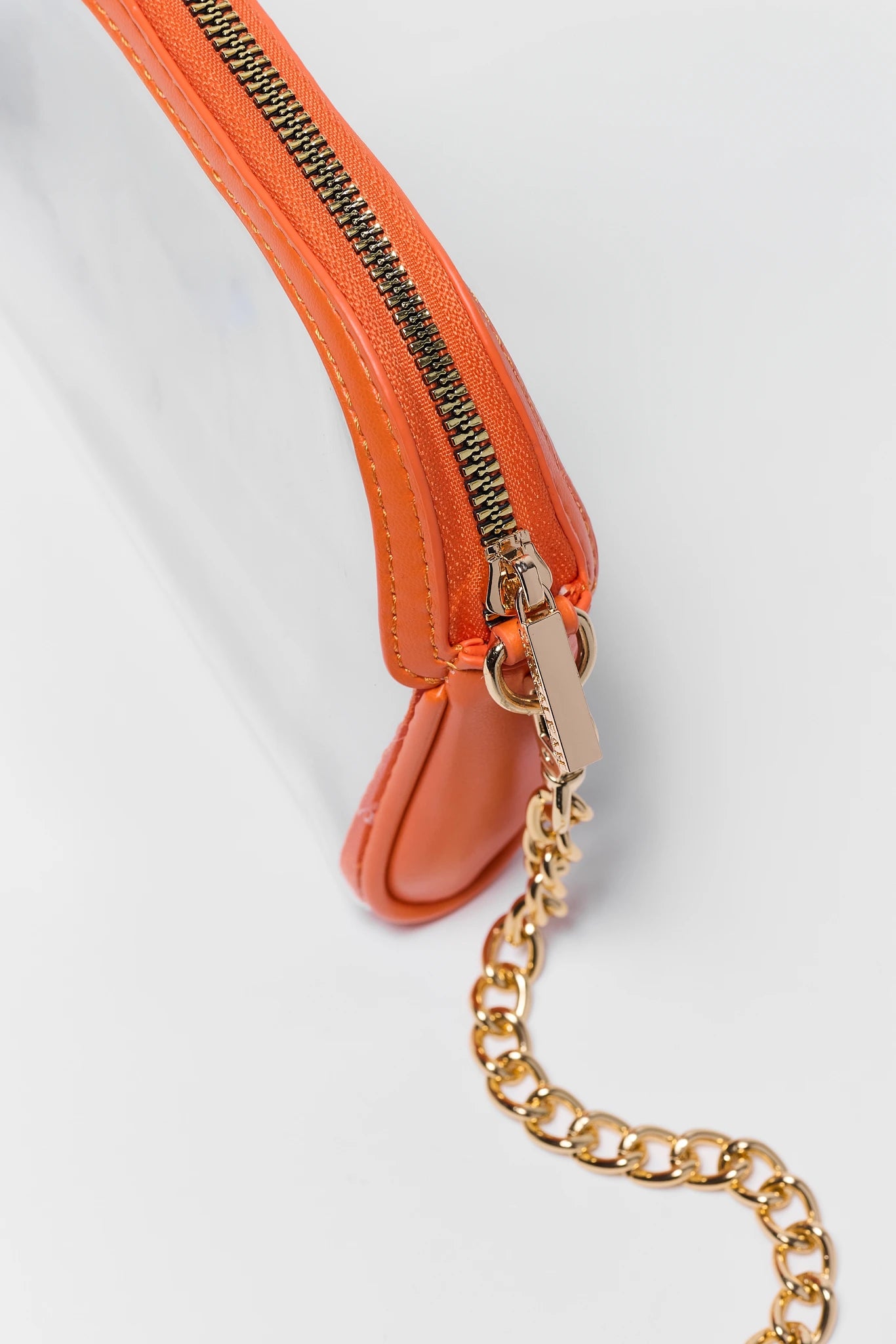 Close-up of a translucent clear bag with a bright orange leather trim and a gold-tone chain strap on a white background.