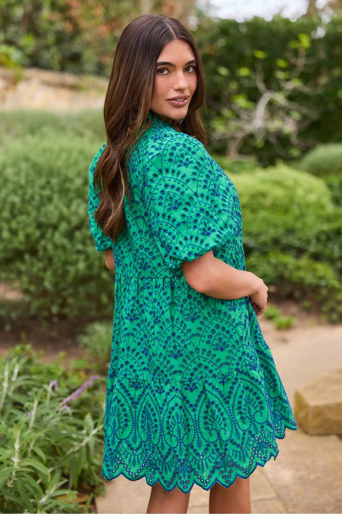 Woman wearing a green lace dress standing outdoors with greenery in the background