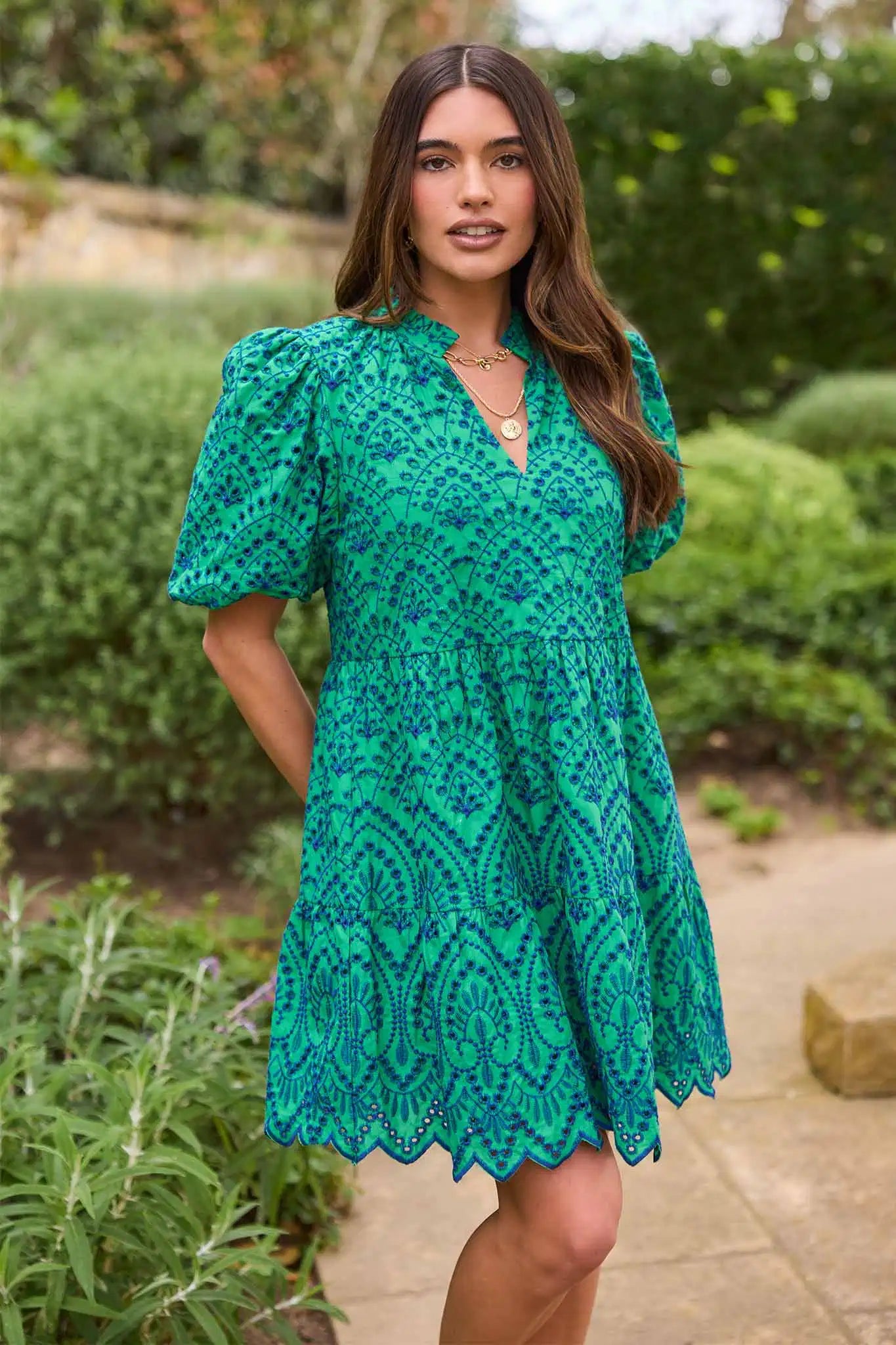 Woman wearing a green patterned dress standing outdoors with greenery in the background