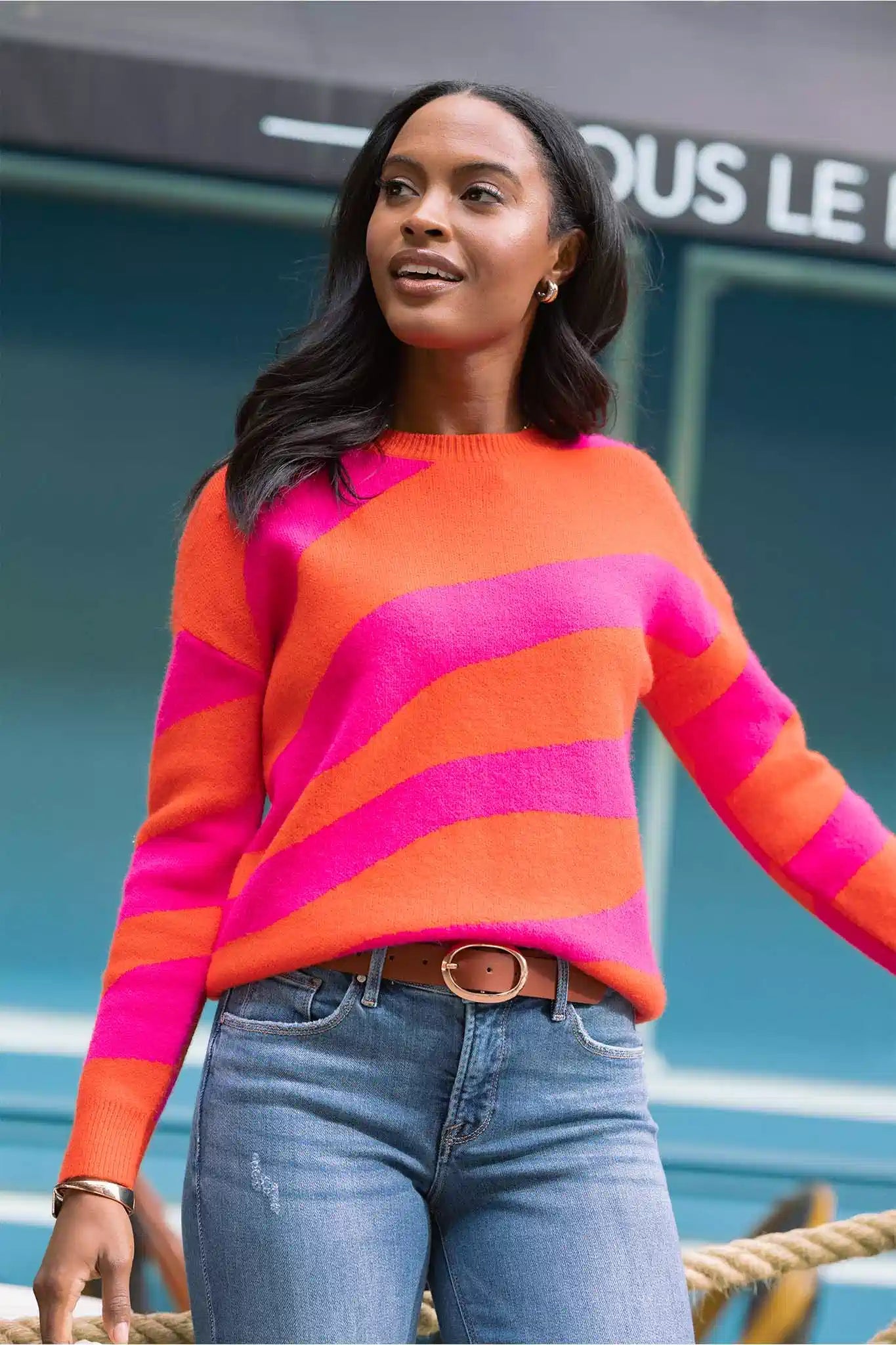Woman wearing a colorful striped sweater and jeans standing outdoors.