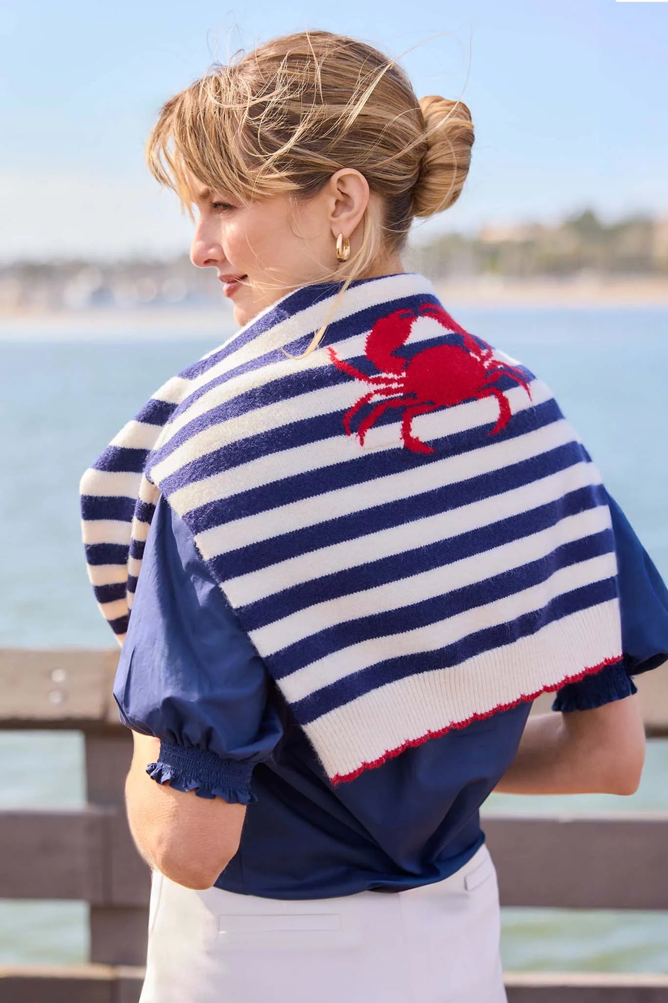 Woman wearing a striped shawl with a red crab design by the water.
