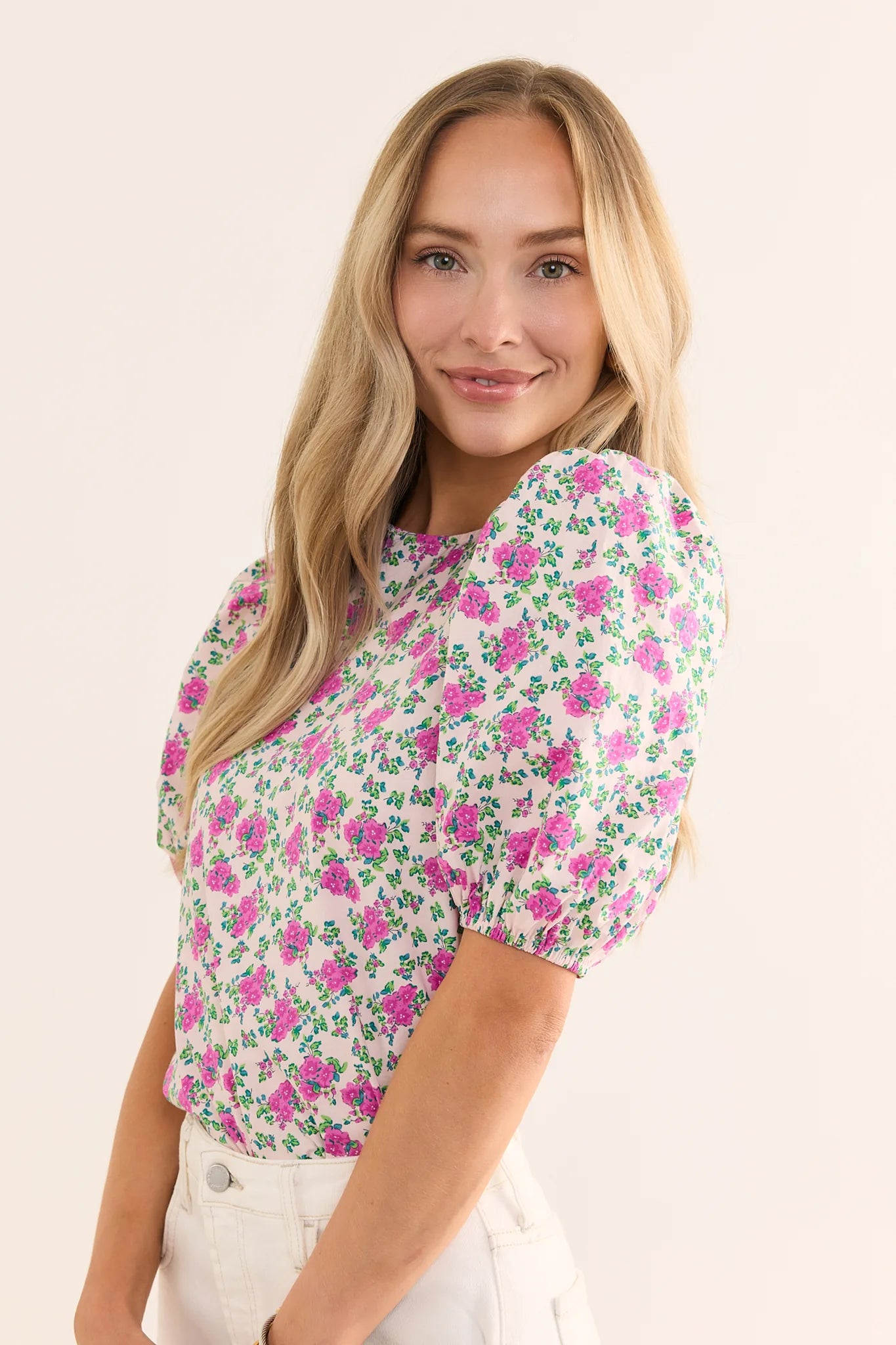 woman wearing pink floral print top on cream background smiling