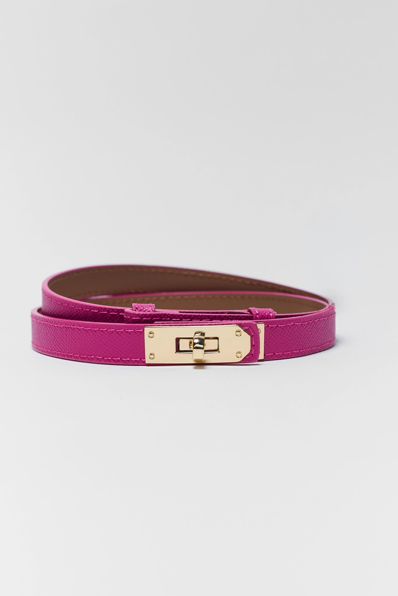 A magenta pink leather belt with a gold-tone turn-lock clasp, coiled on a light gray background.