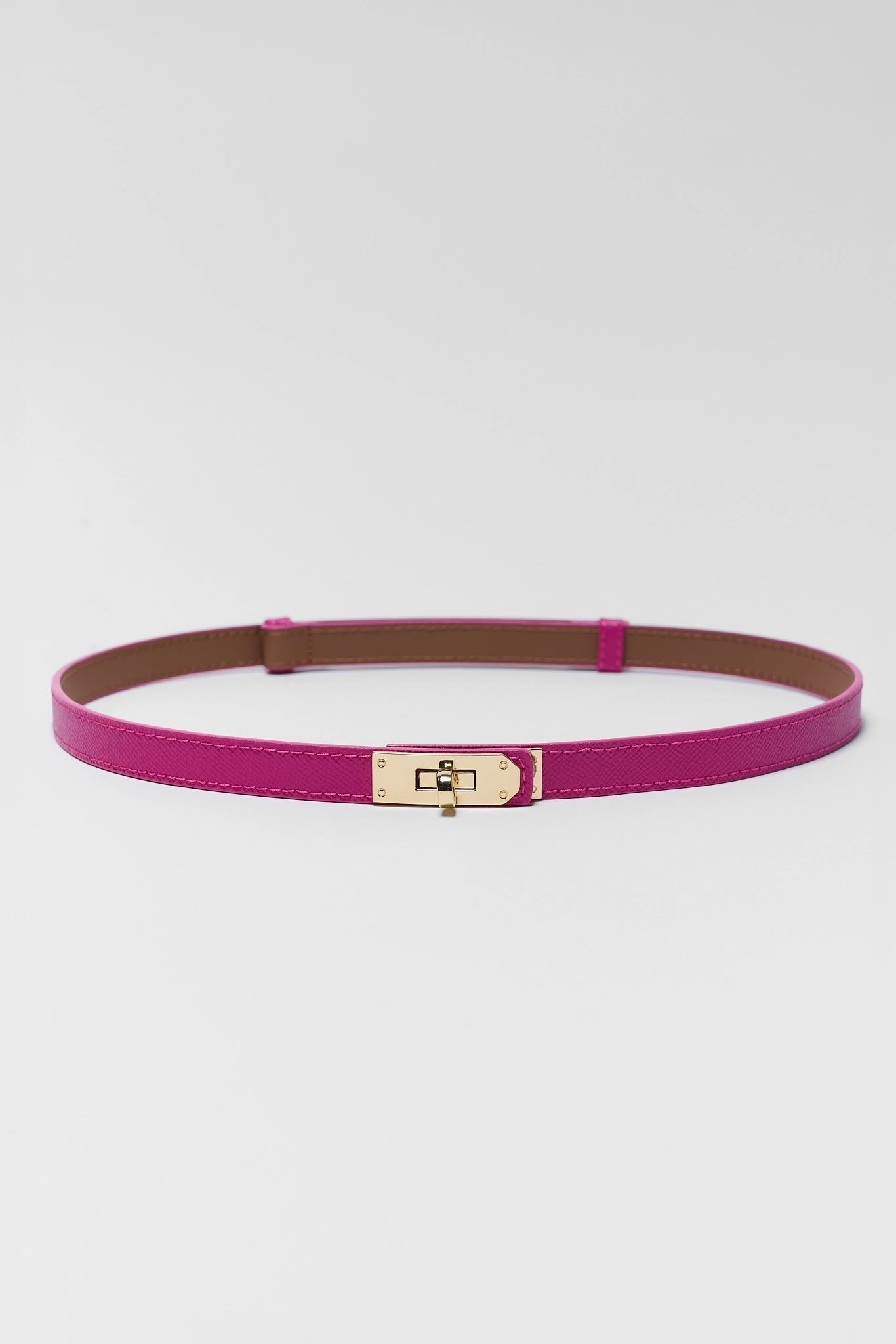 A slim magenta pink leather belt with a gold-tone metal turn-lock clasp, displayed horizontally on a light gray background.