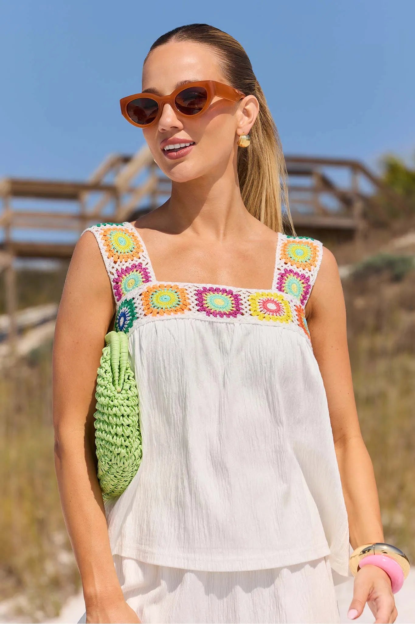 Woman in a colorful top and white dress with sunglasses on a beach.