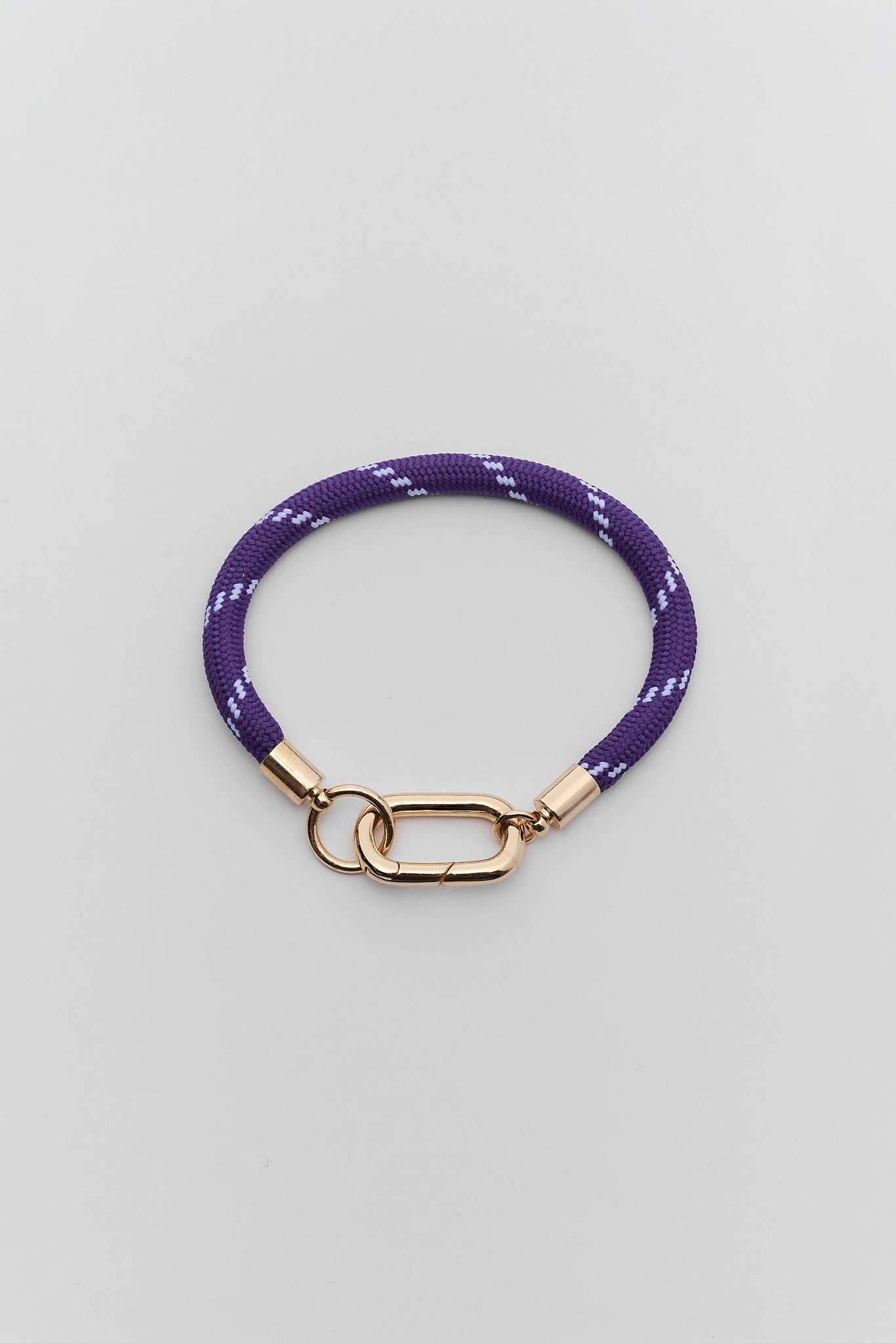A purple woven rope bracelet with a gold-tone lobster clasp, displayed on a neutral light gray background.