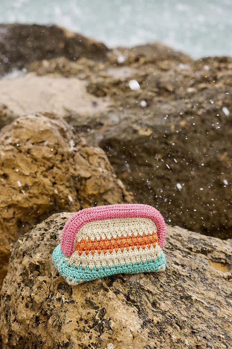 Crocheted striped bar of soap on a rock with water in the background