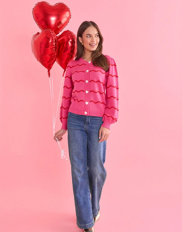 Woman in a pink sweater with heart patterns holding red heart-shaped balloons on a pink background
