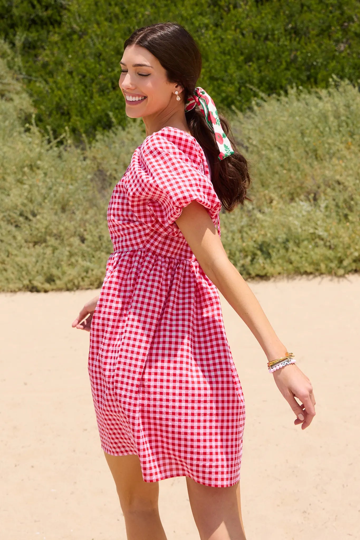 Woman in a red and white checkered dress standing outdoors with greenery in the background