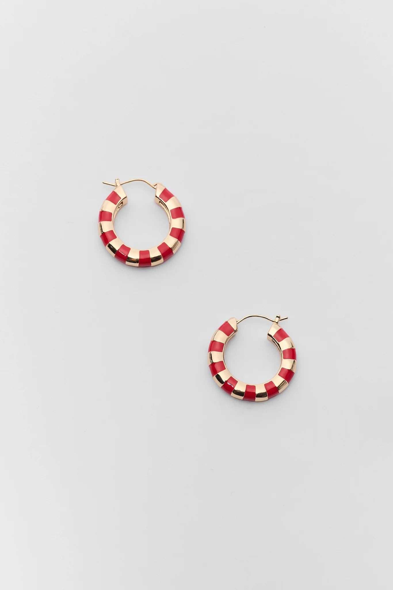 A pair of gold hoop earrings with a red and white checkered pattern, displayed on a light gray background.