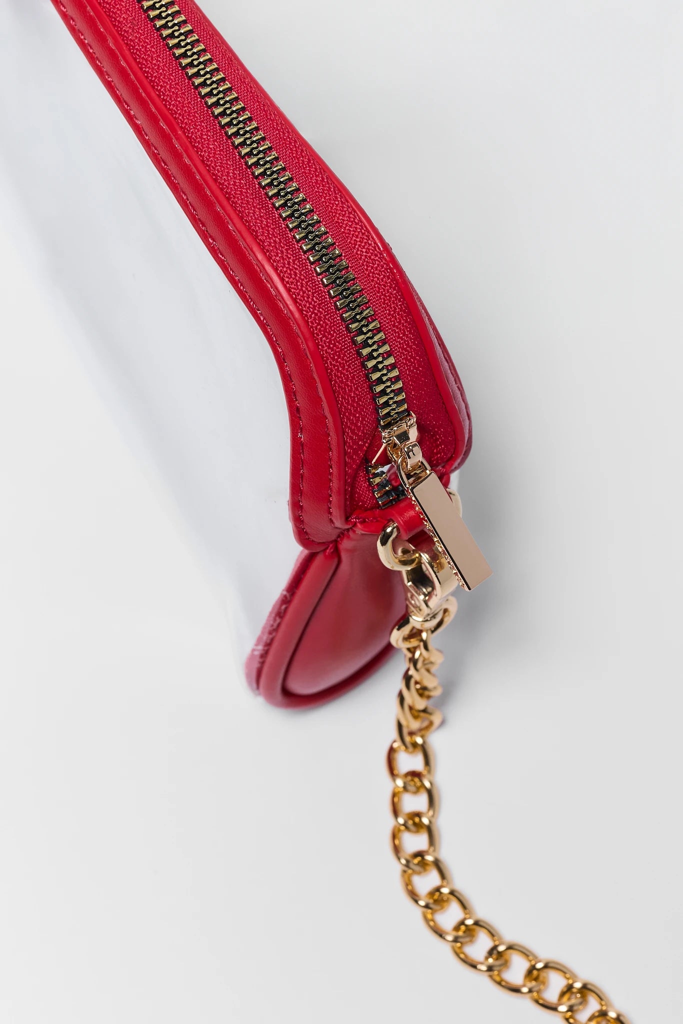 Close-up of a red leather zippered pouch with a gold-tone metal zipper pull and a gold chain strap, shown on a light gray background.