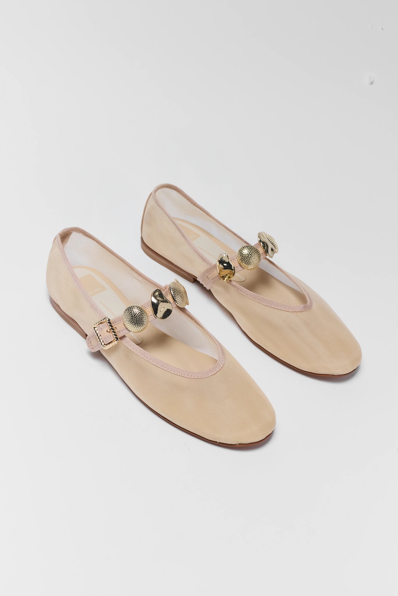 Pair of beige flat shoes with gold buckles on a white background