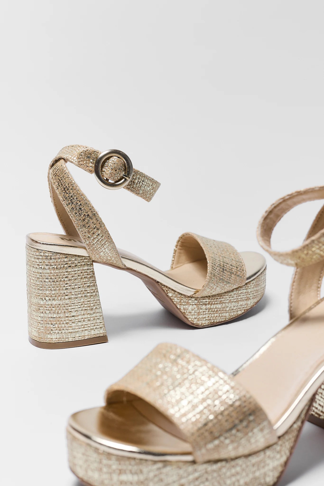 Pair of gold glittery platform sandals on a light gray background