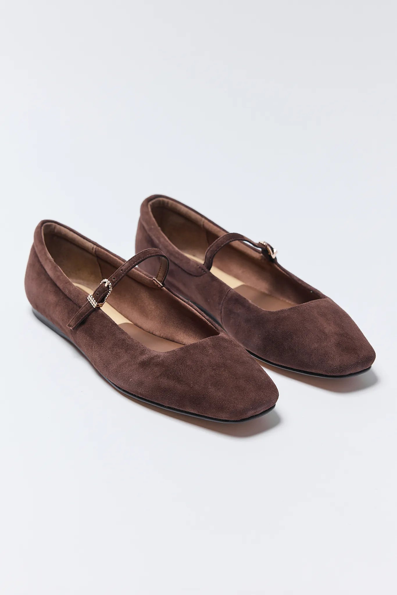 Pair of brown suede Reyes Ballet Flats with a strap on a light gray background