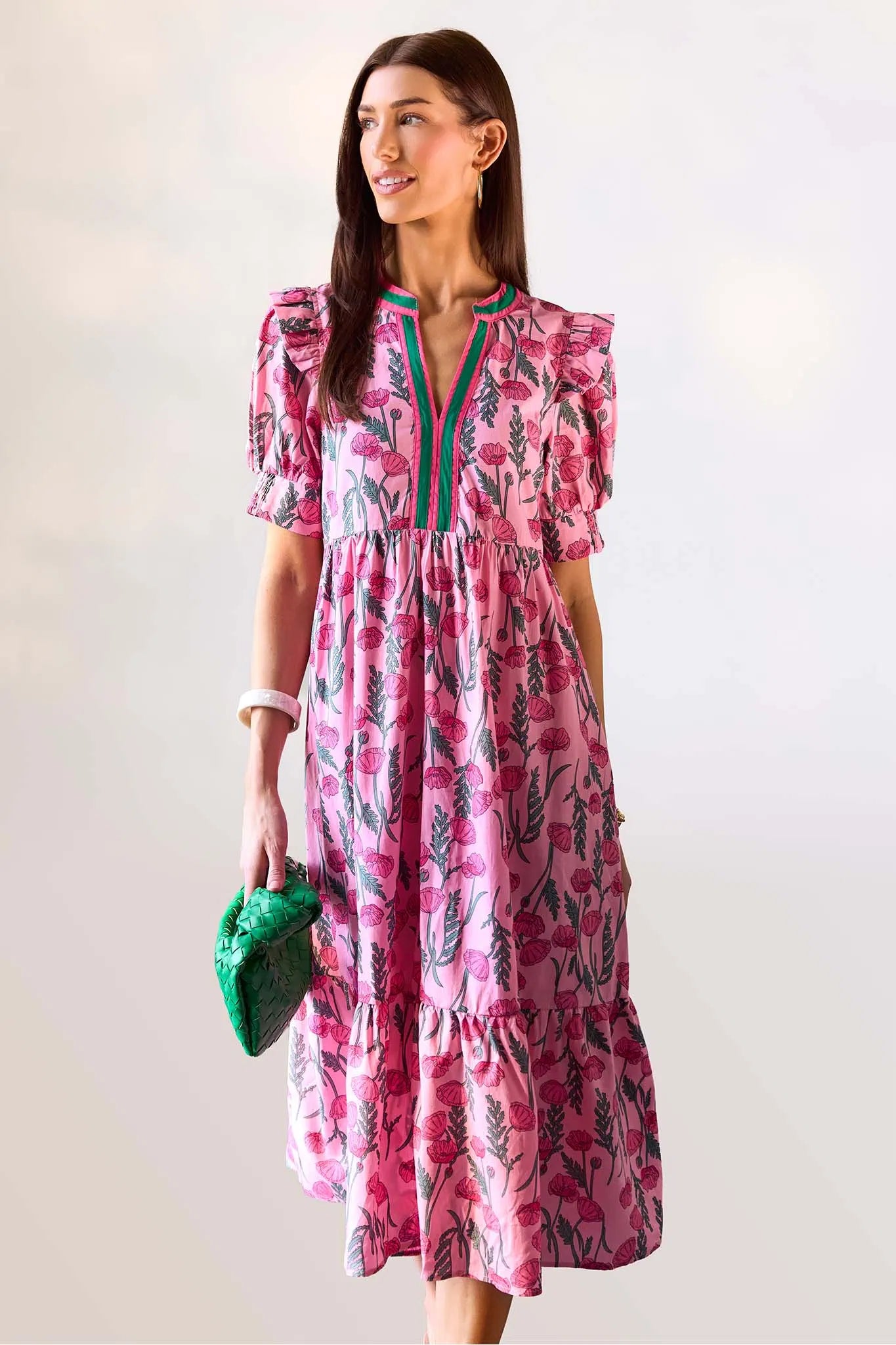 Woman wearing a pink floral dress with a green clutch against a white background