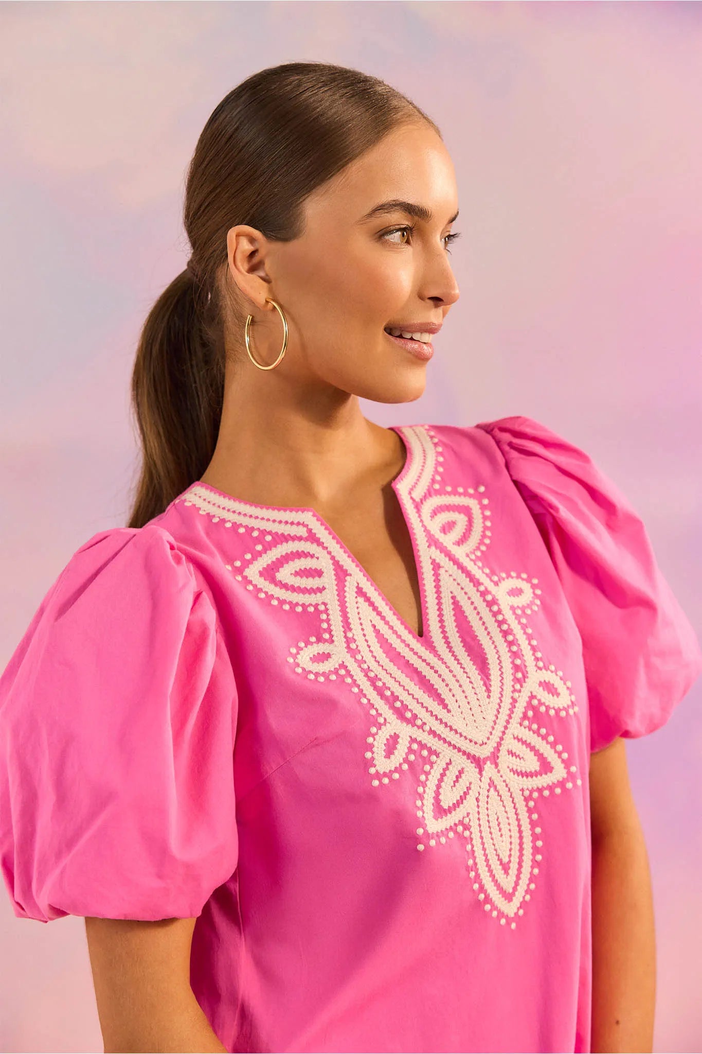 Woman wearing a pink blouse with white embroidery against a soft pink background