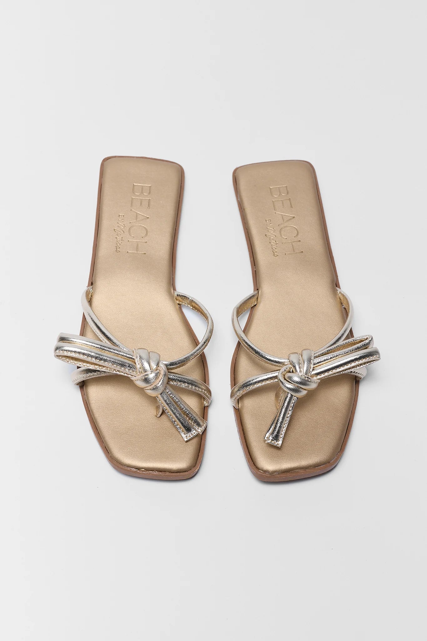 two Pair of gold sandals with silver straps on a light gray background