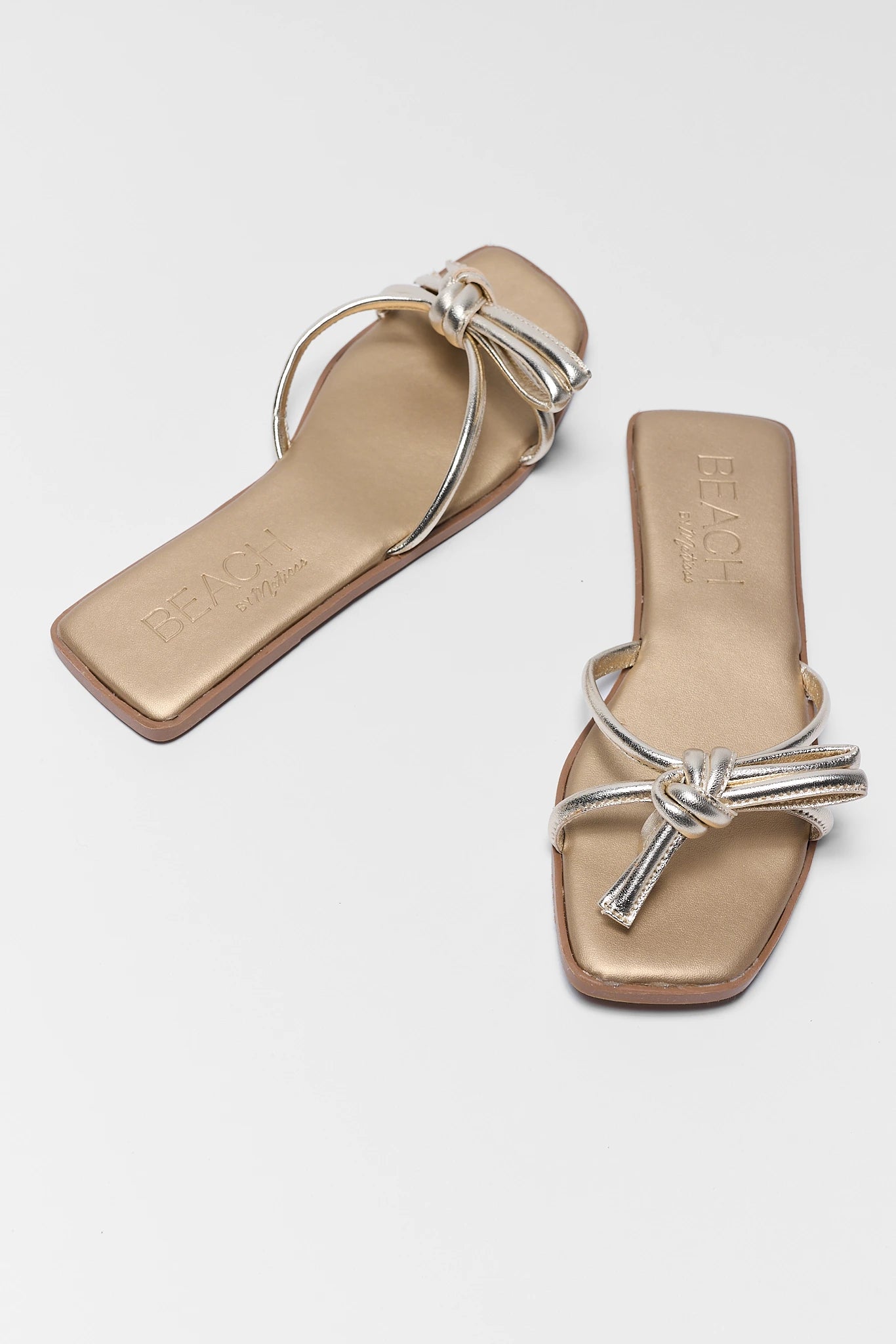 Pair of beige sandals with silver straps on a light gray background