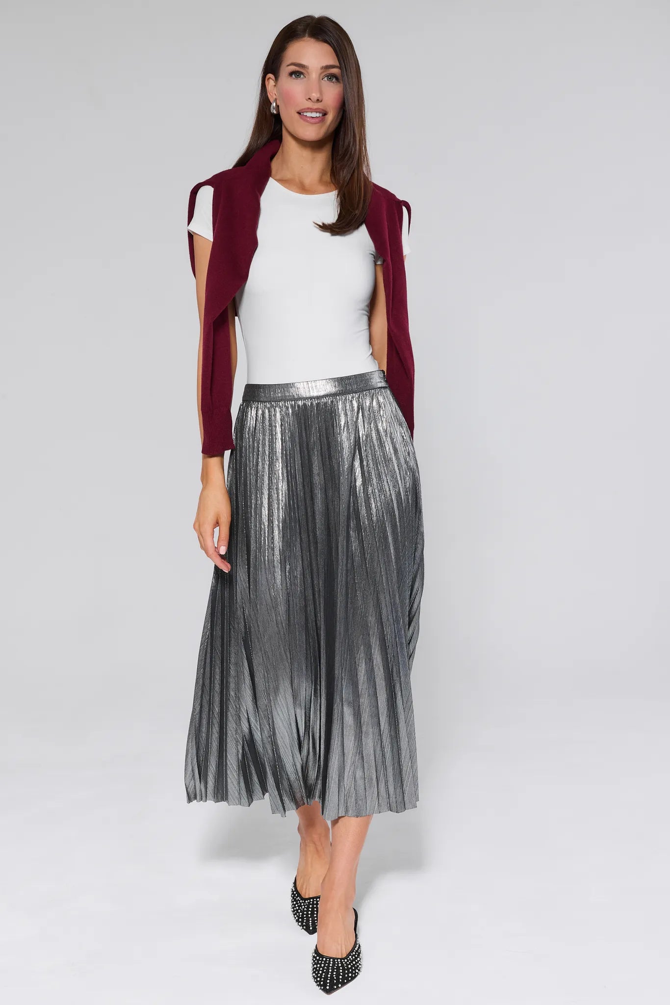 Woman wearing a Hensley Silver Pleated Midi Skirt with a white top and red jacket on a gray background