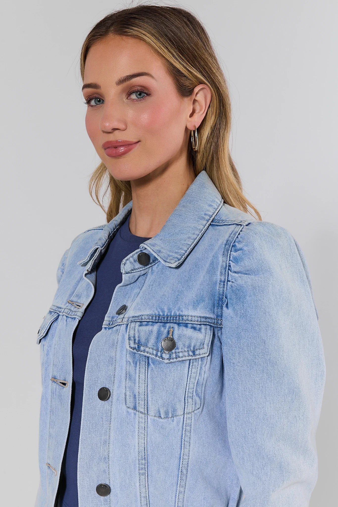 Woman wearing a light blue denim jacket against a plain background