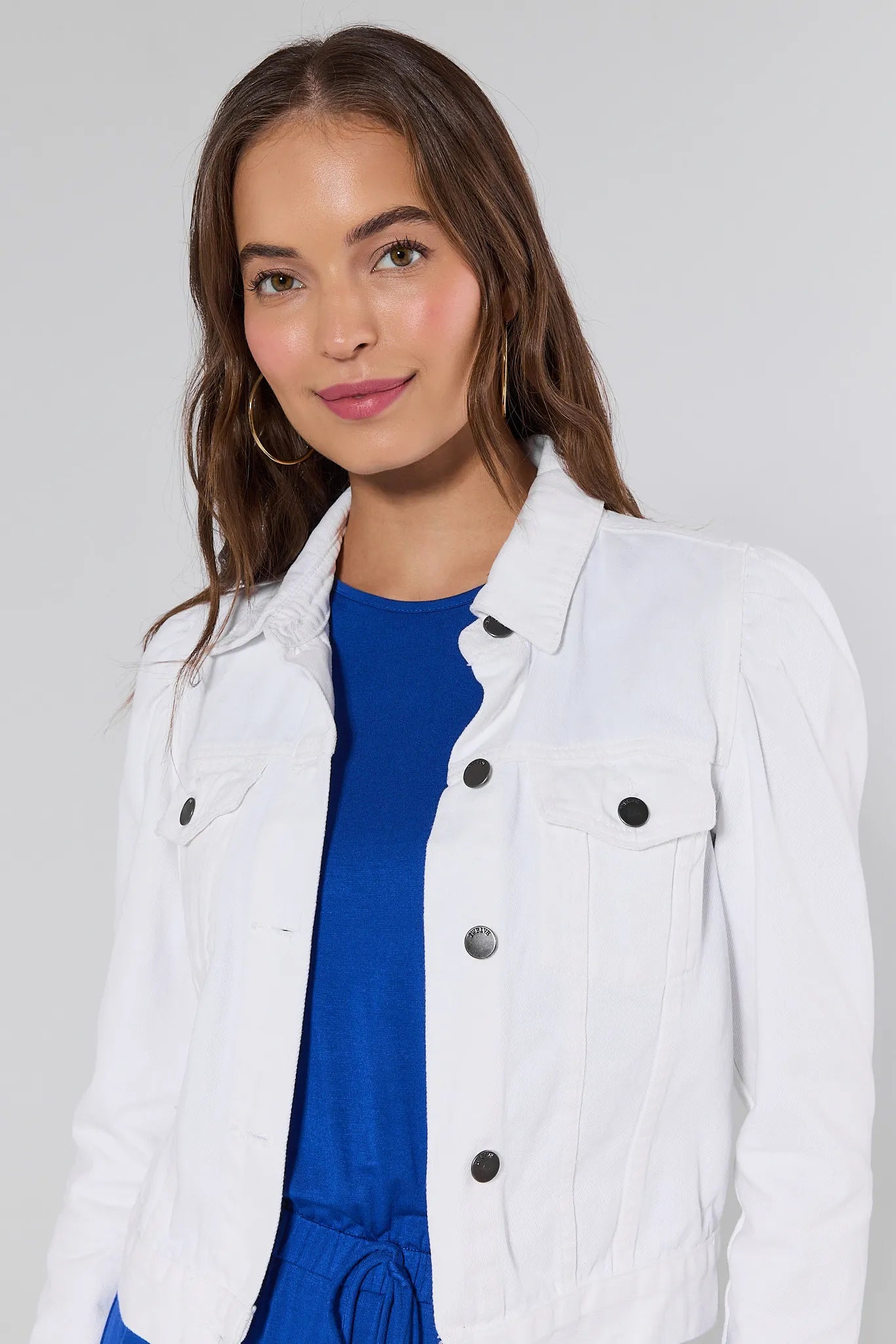 Woman wearing a white jacket over a blue top on a plain background