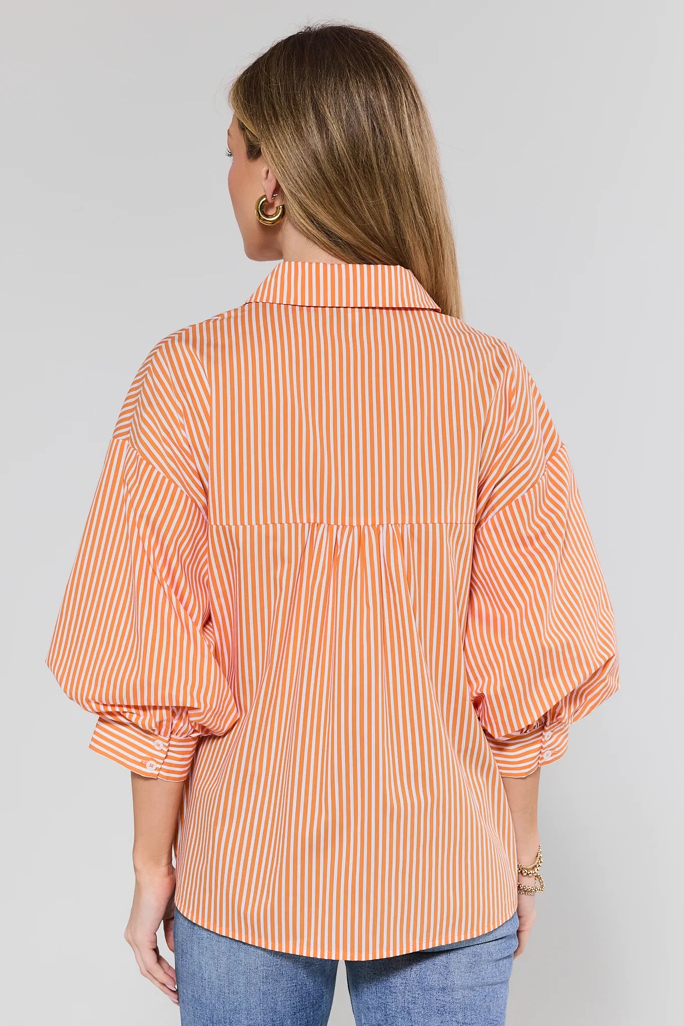 Woman wearing Susan Orange Striped Puff Sleeve Top with balloon sleeves, paired with medium-wash jeans, gold hoop earrings, and bracelet stack. Relaxed, hip-length fit.
