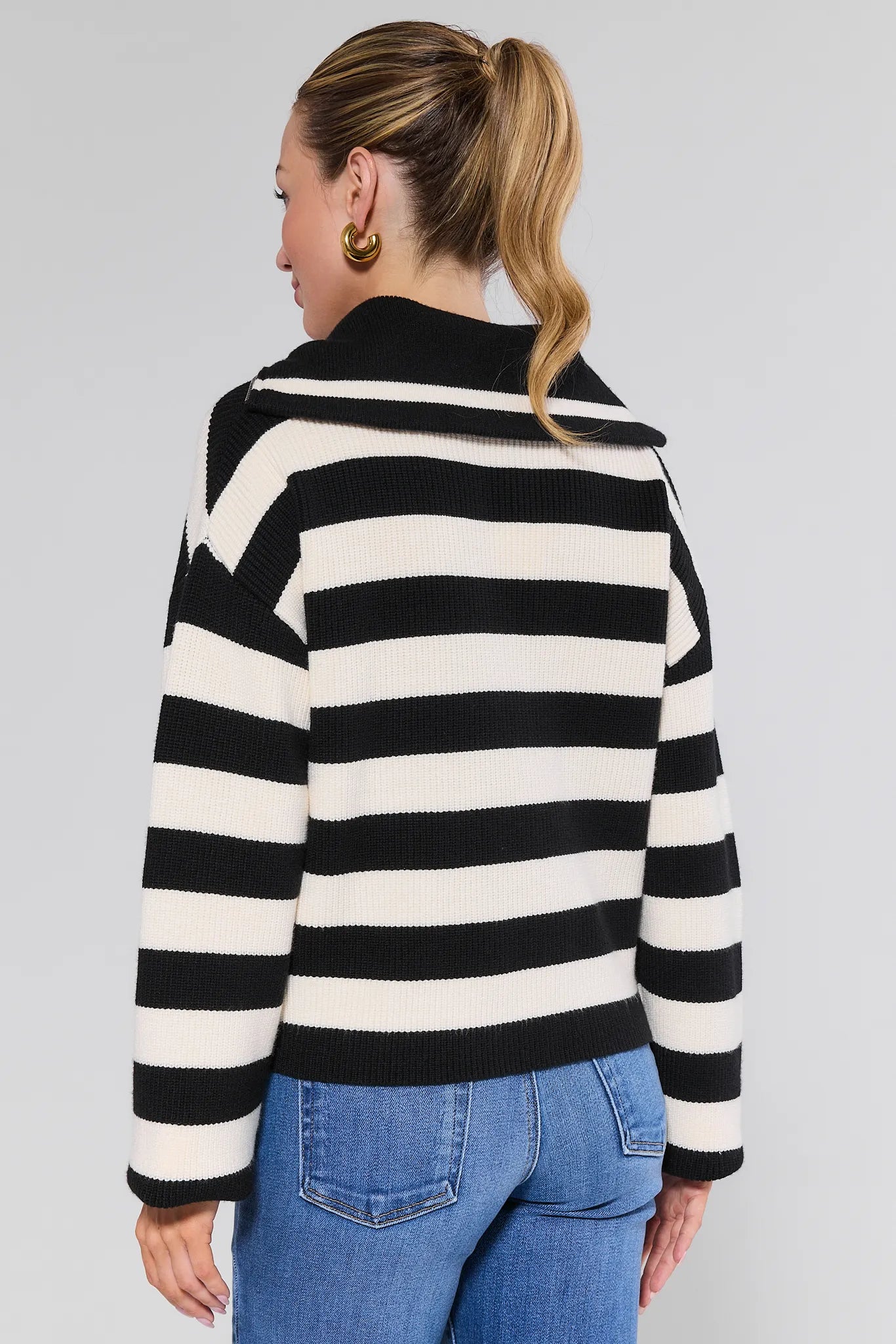 Person wearing a black and white striped Cheryl Sweater with blue jeans on a plain background