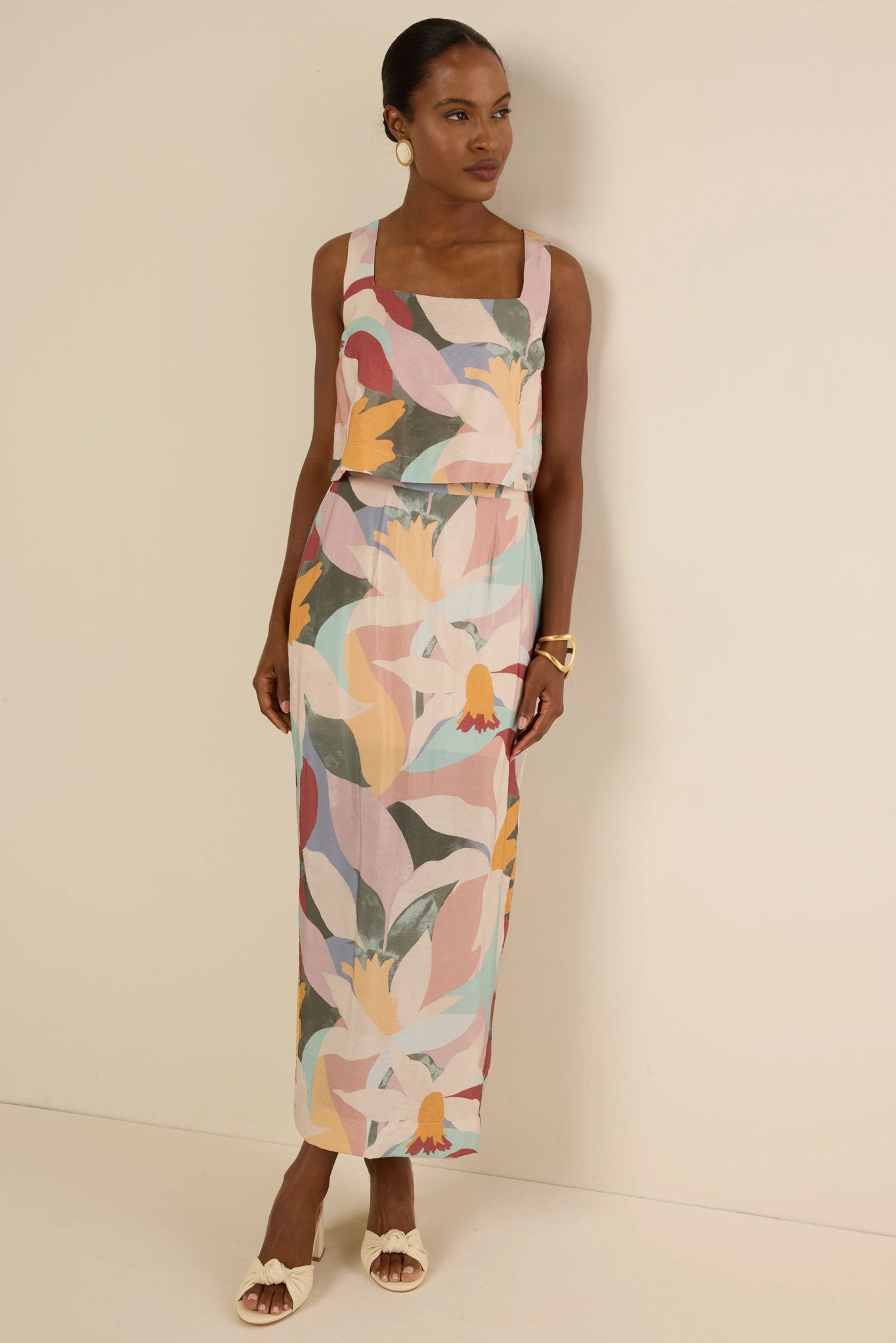 Woman wearing the Elliana Skirt with abstract floral print, square neckline, and column silhouette; paired with cream sandals, gold hoop earrings, and cuff bracelet.