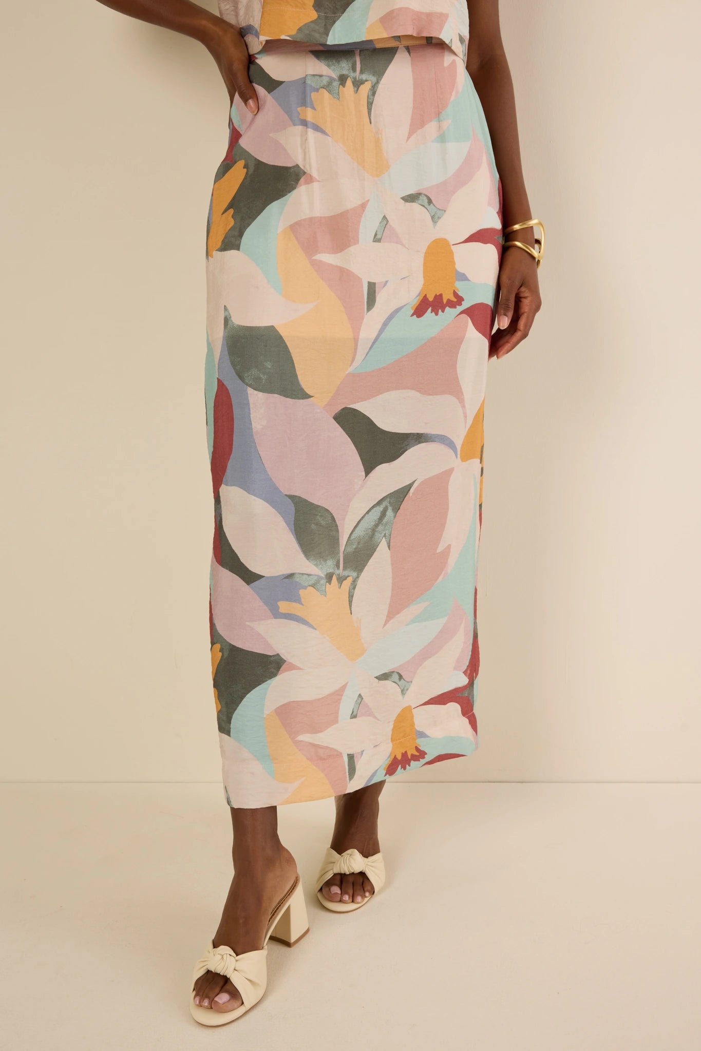 Person wearing the Elliana Skirt with abstract florals, paired with cream knotted mules. Skirt features elastic waist, back slit, and shift silhouette.