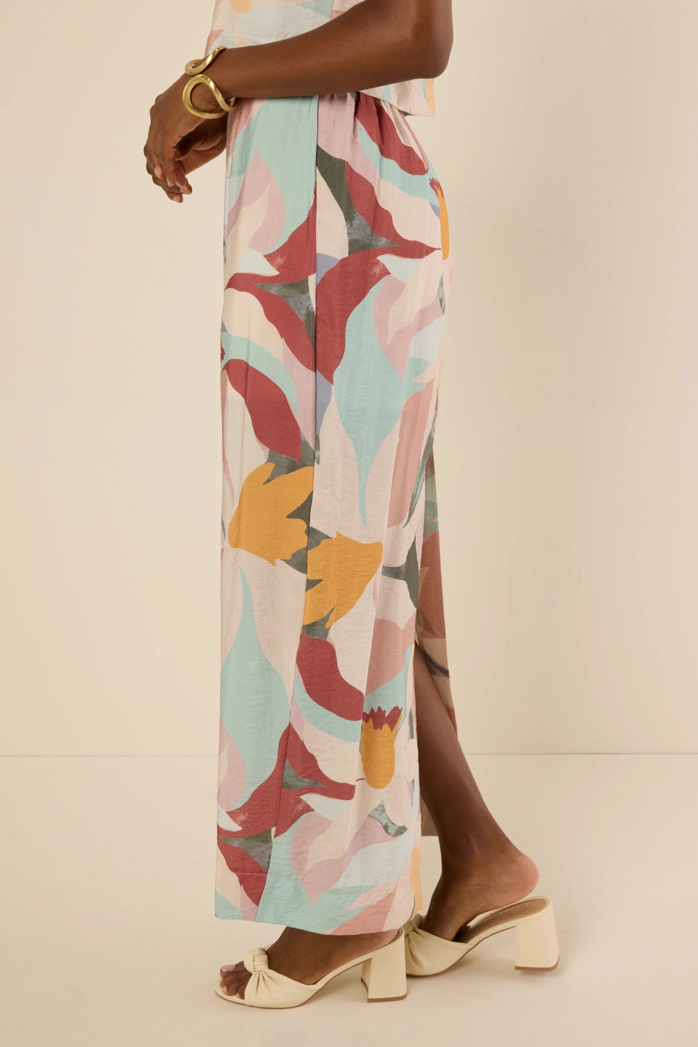 Model wears Elliana Skirt in bold abstract floral print, paired with cream block-heel mules and a gold bangle, highlighting its lightweight, full-length shift silhouette.