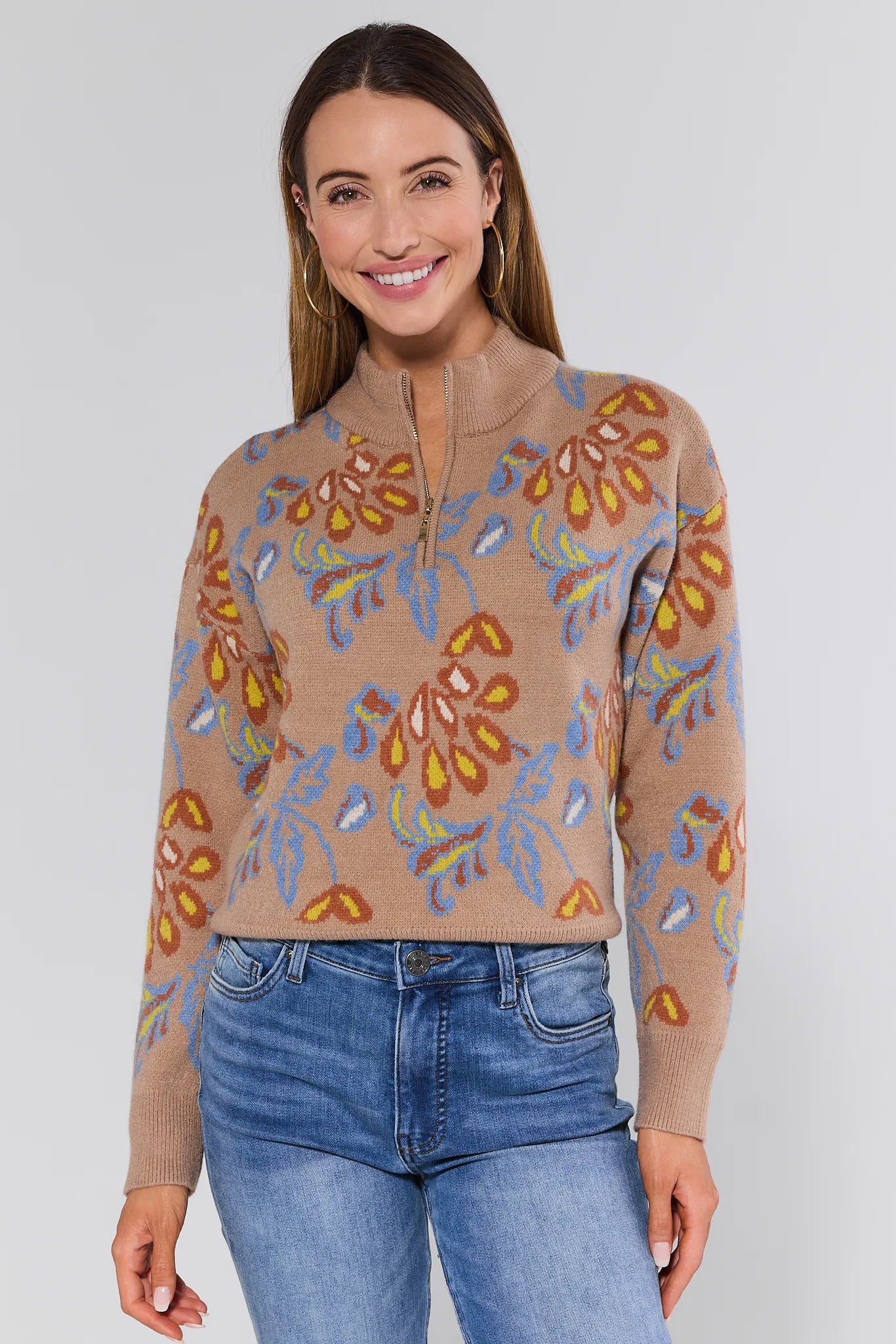 Woman wearing a beige Nancy Sweater with floral patterns and blue jeans on a white background