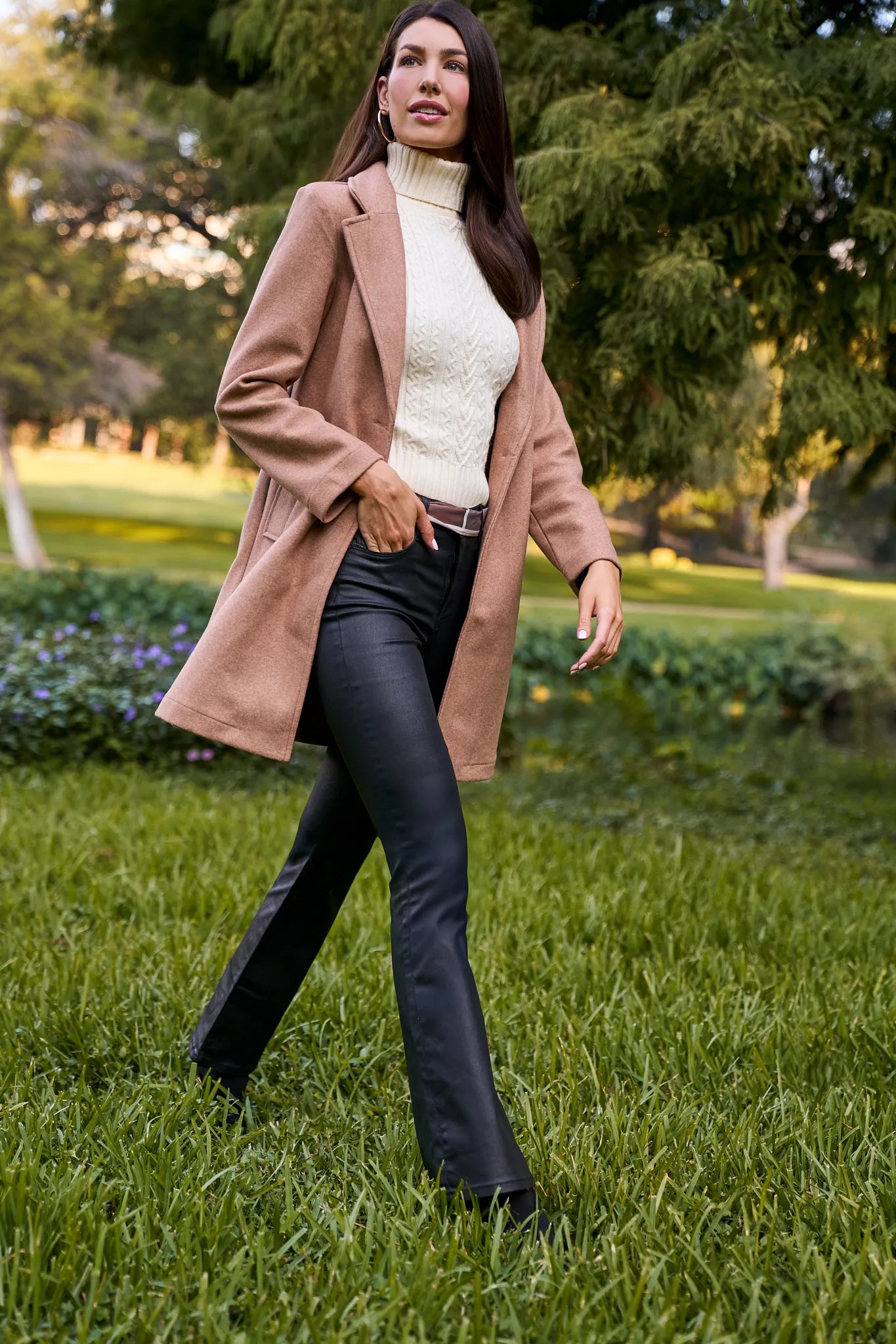 Woman in a beige coat and black Ana Jeans Wax Coated standing in a park.