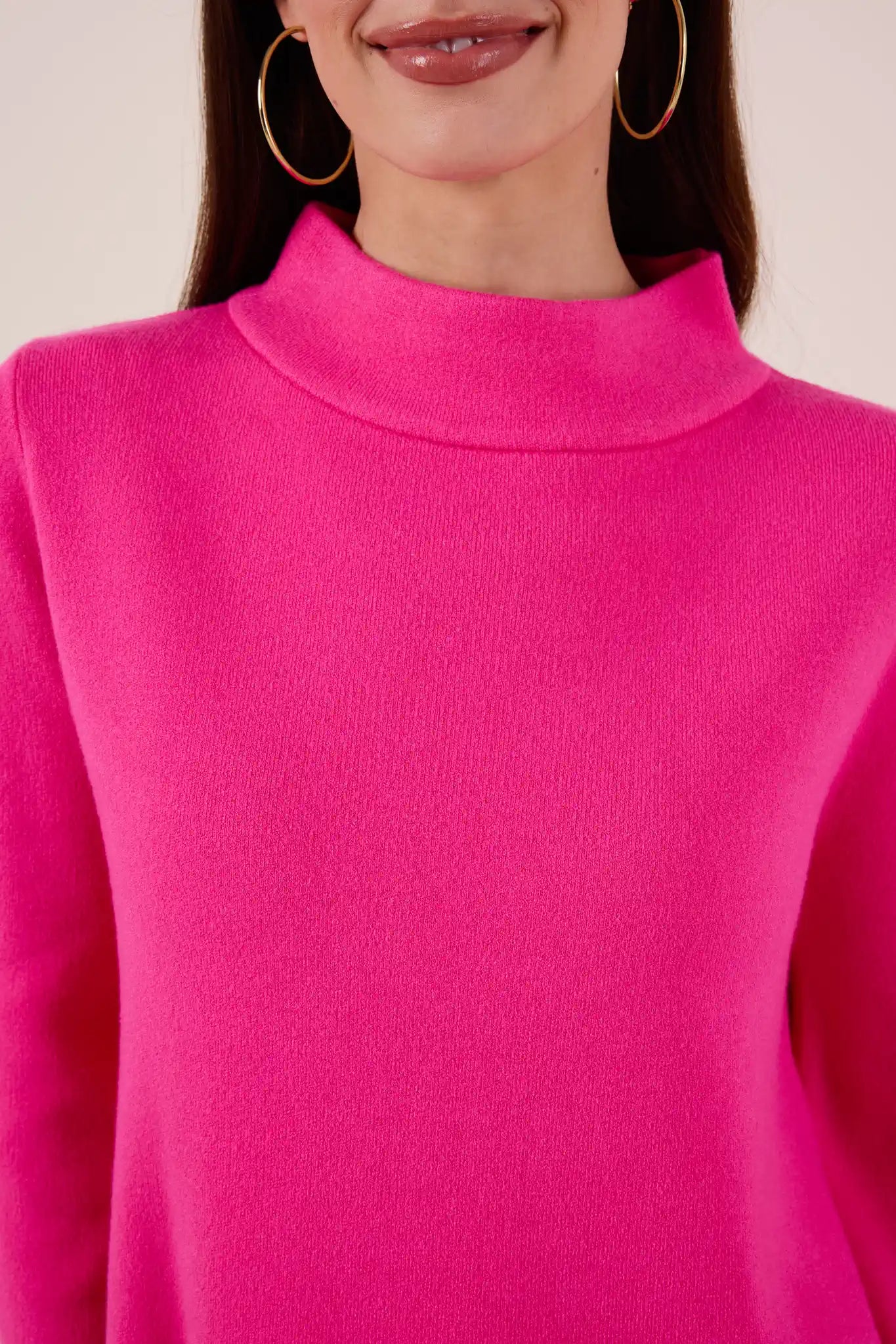 Close-up of a person wearing a bright pink Jackie sweater with a plain background