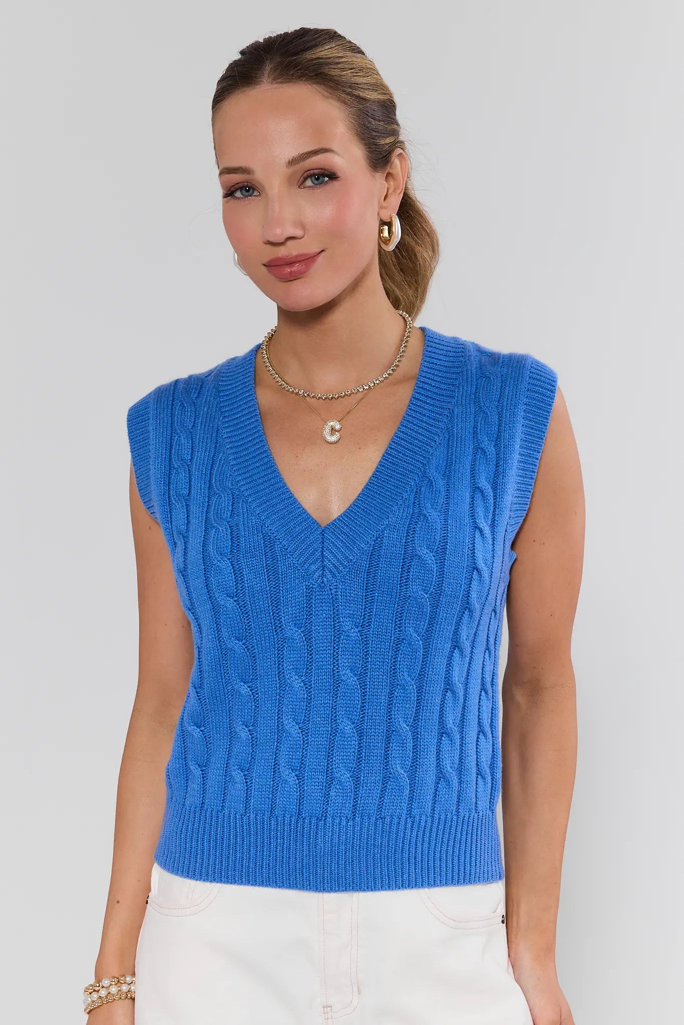Woman wearing a blue sleeveless knitted top against a plain background