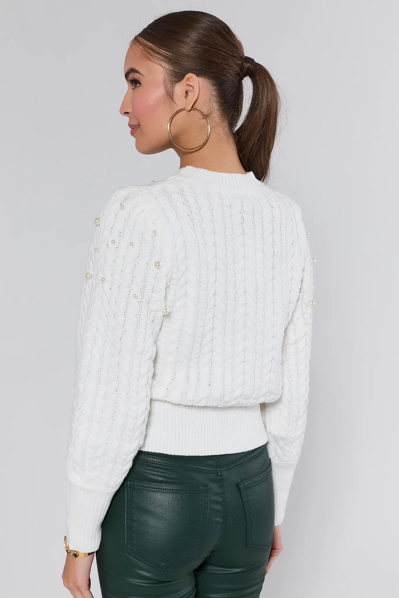 Woman wearing a white Bailey sweater and green pants on a plain background