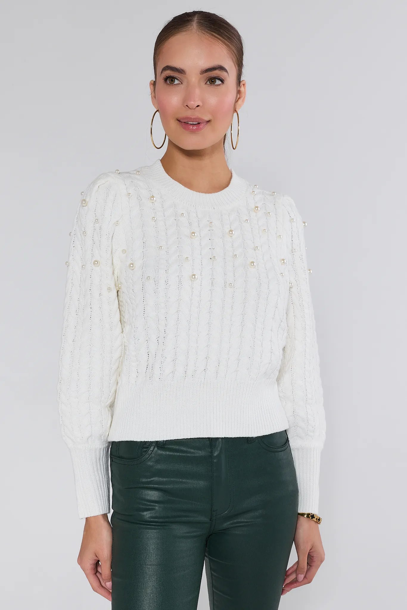 Woman wearing a white Bailey sweater and green pants on a plain background