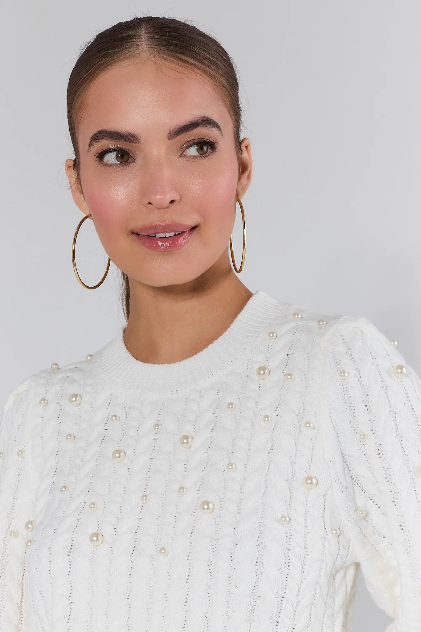 Woman wearing a white Bailey sweater and green pants on a plain background