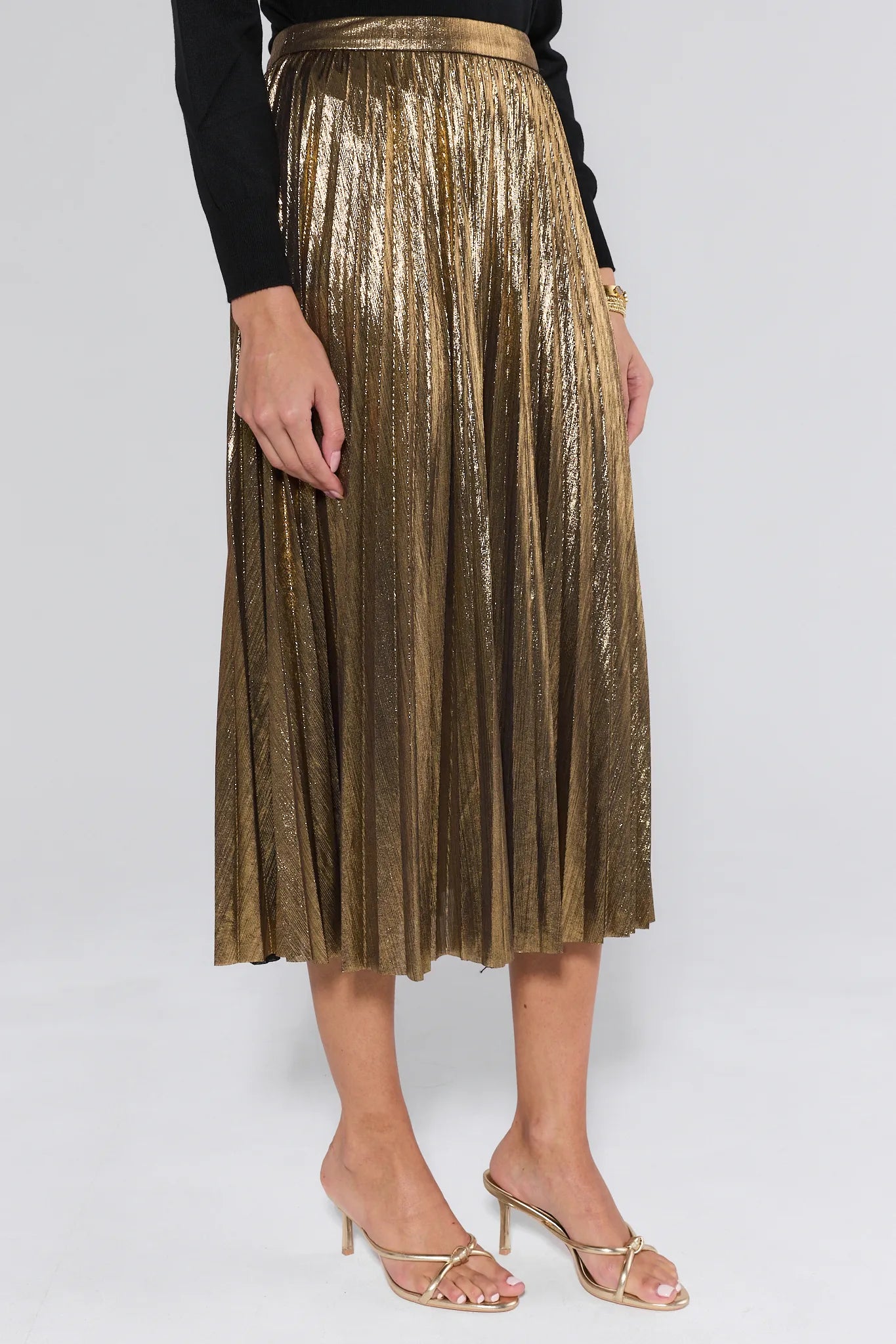 Gold pleated skirt worn by a person on a white background