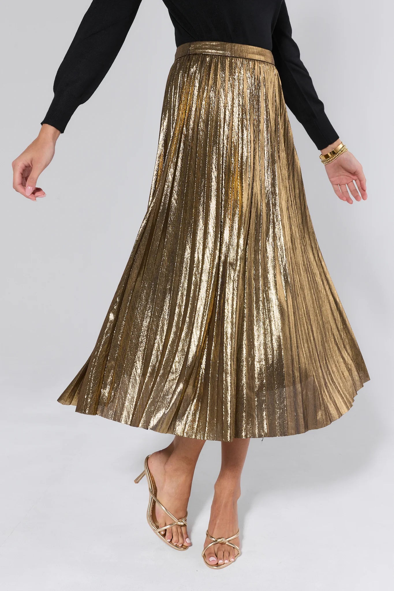 Gold pleated skirt worn by a person on a white background