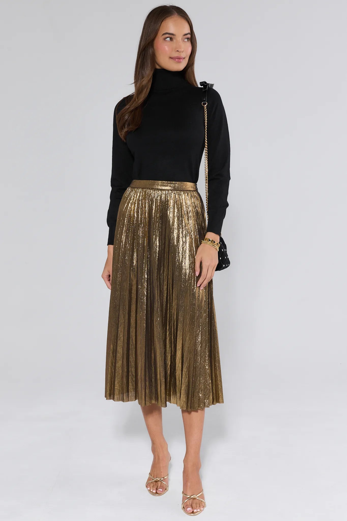 Woman wearing a black top and gold pleated skirt on a white background
