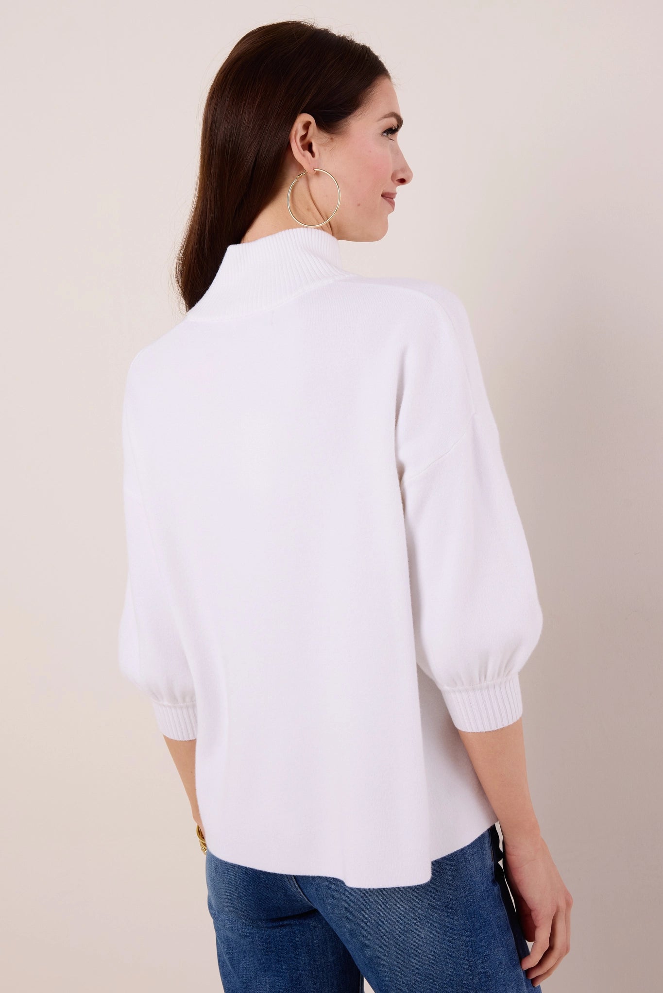 Woman wearing a white Gwyneth sweater and blue jeans against a beige background