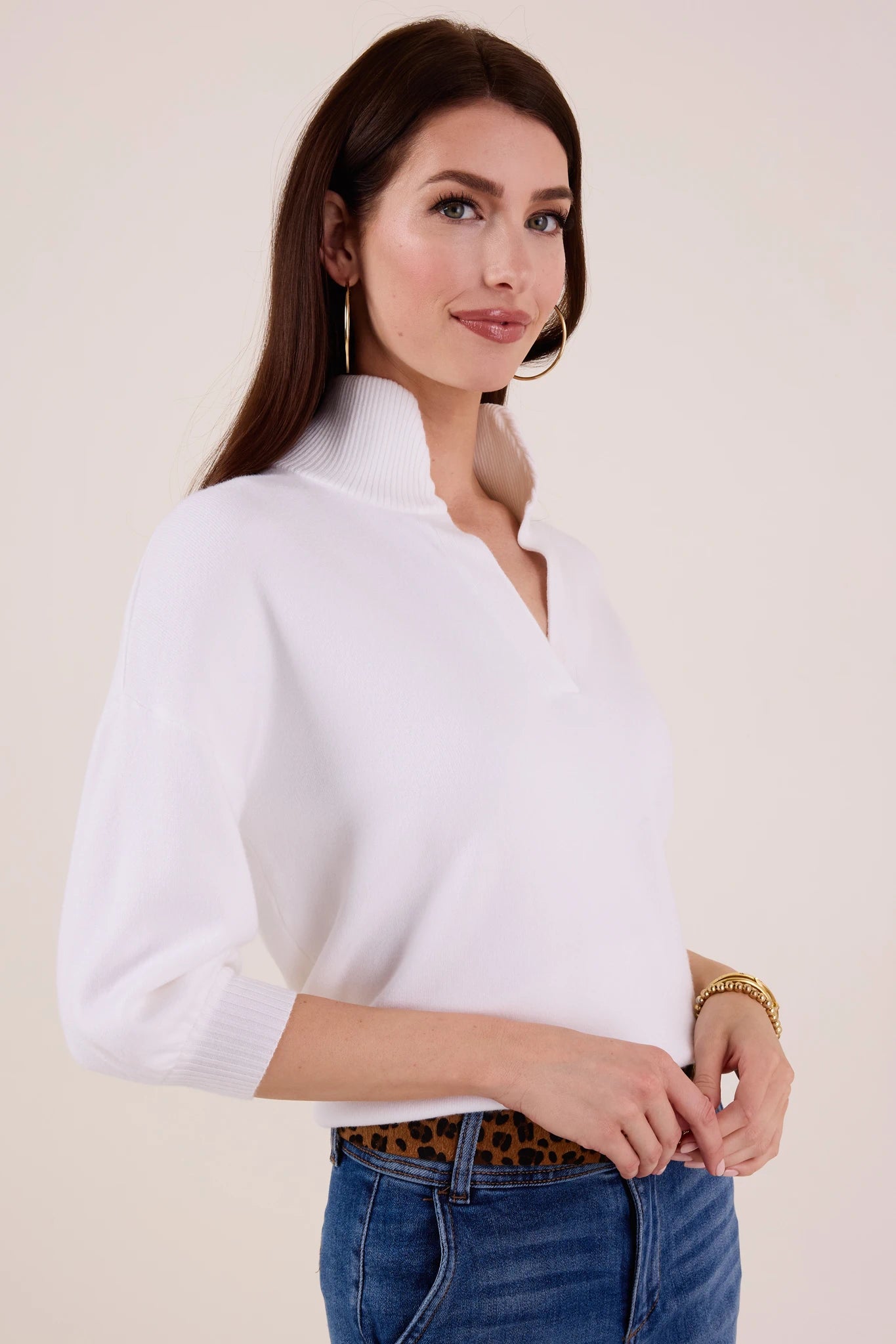 Woman wearing a white Gwyneth sweater and blue jeans against a plain background